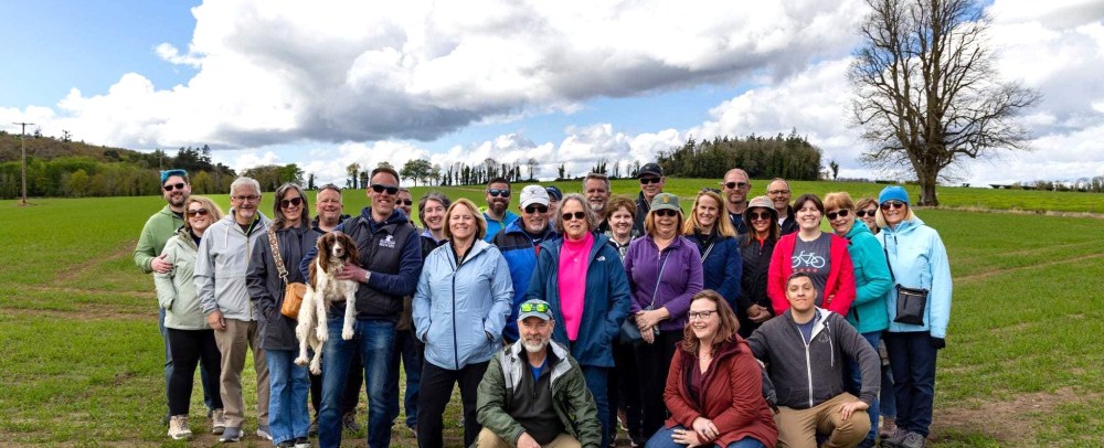 Group of people and a dog posing in a grassy field under a cloudy sky.