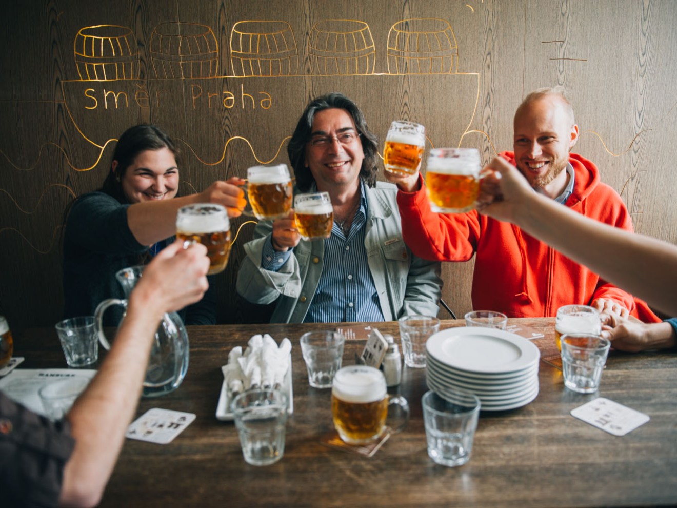 Group of people sitting at a table toasting with beer glasses in a pub.