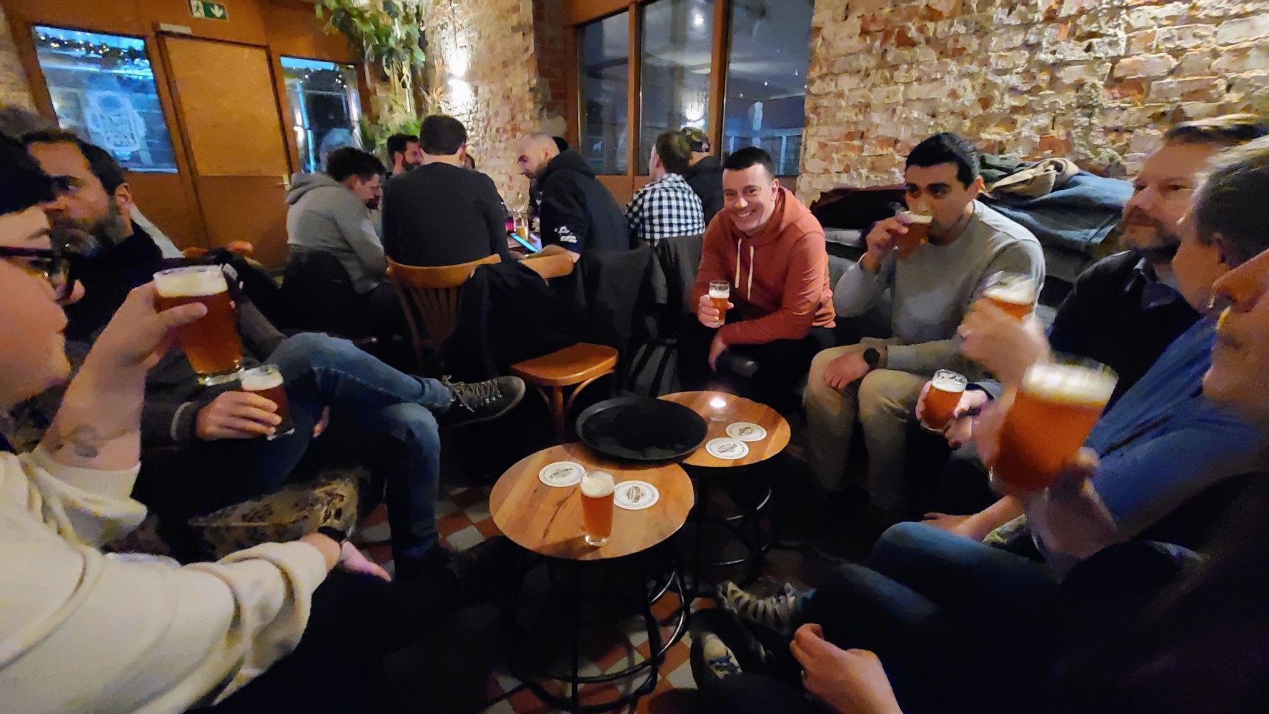 Group of people sitting with drinks in a cozy bar with brick walls.