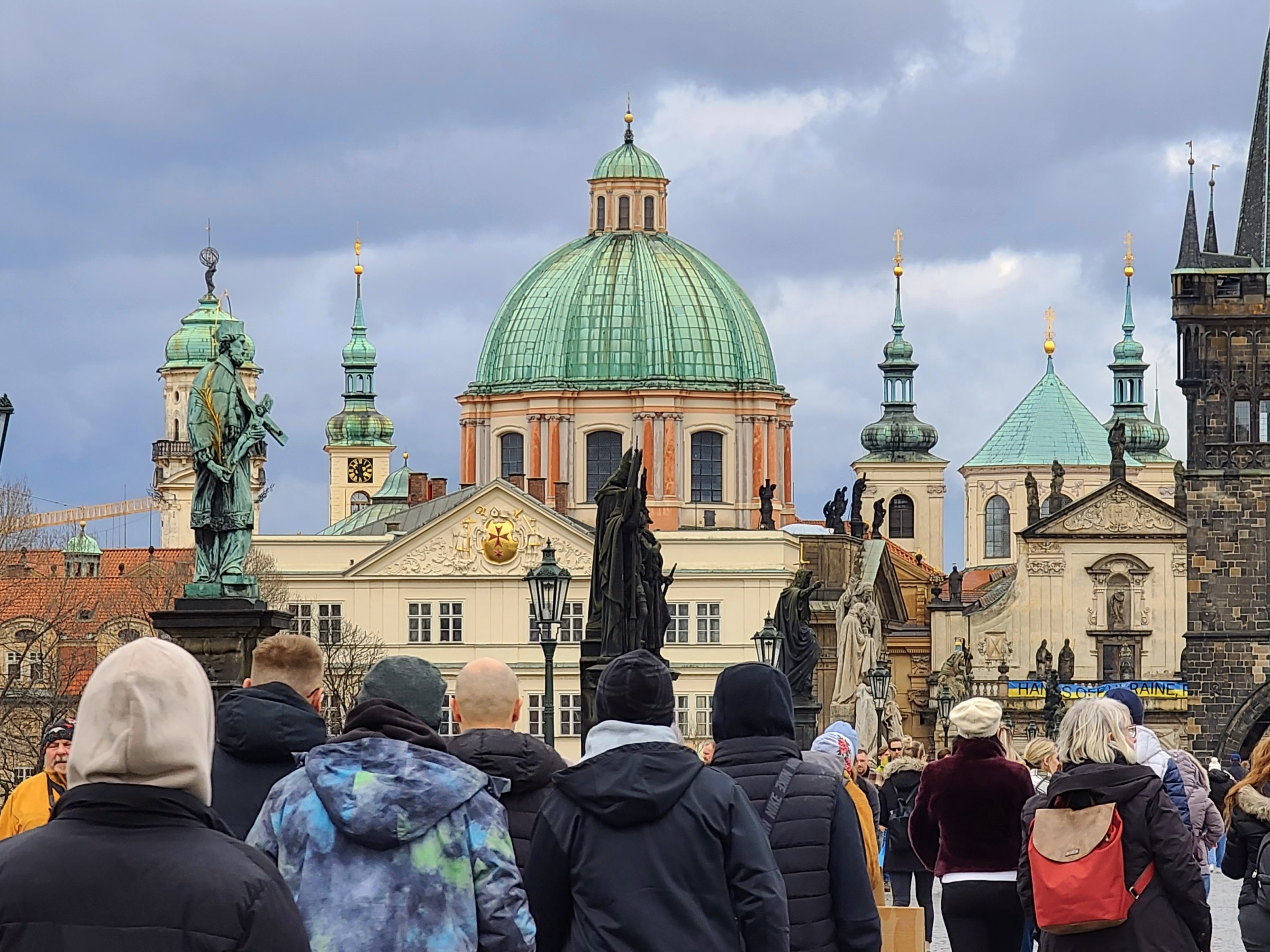 Crowd of people on a bridge with historic architectural dome and towers in the background.