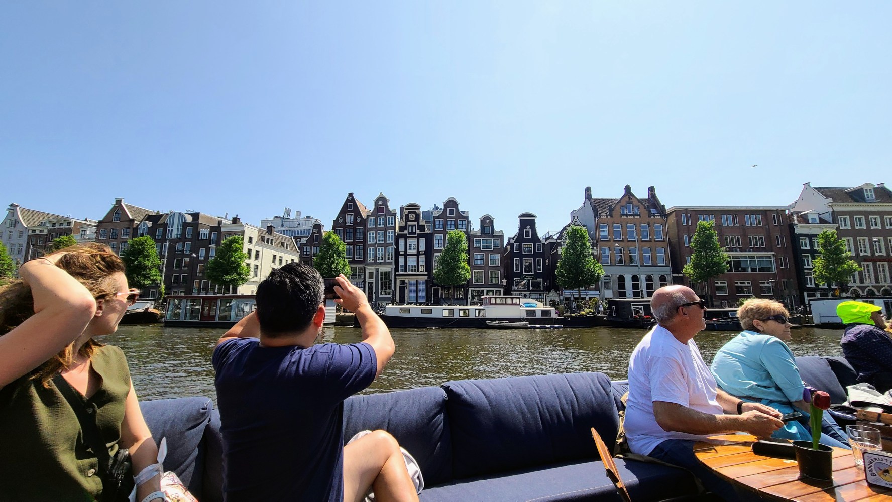 People on a boat enjoying a view of Amsterdam canal houses on a sunny day.
