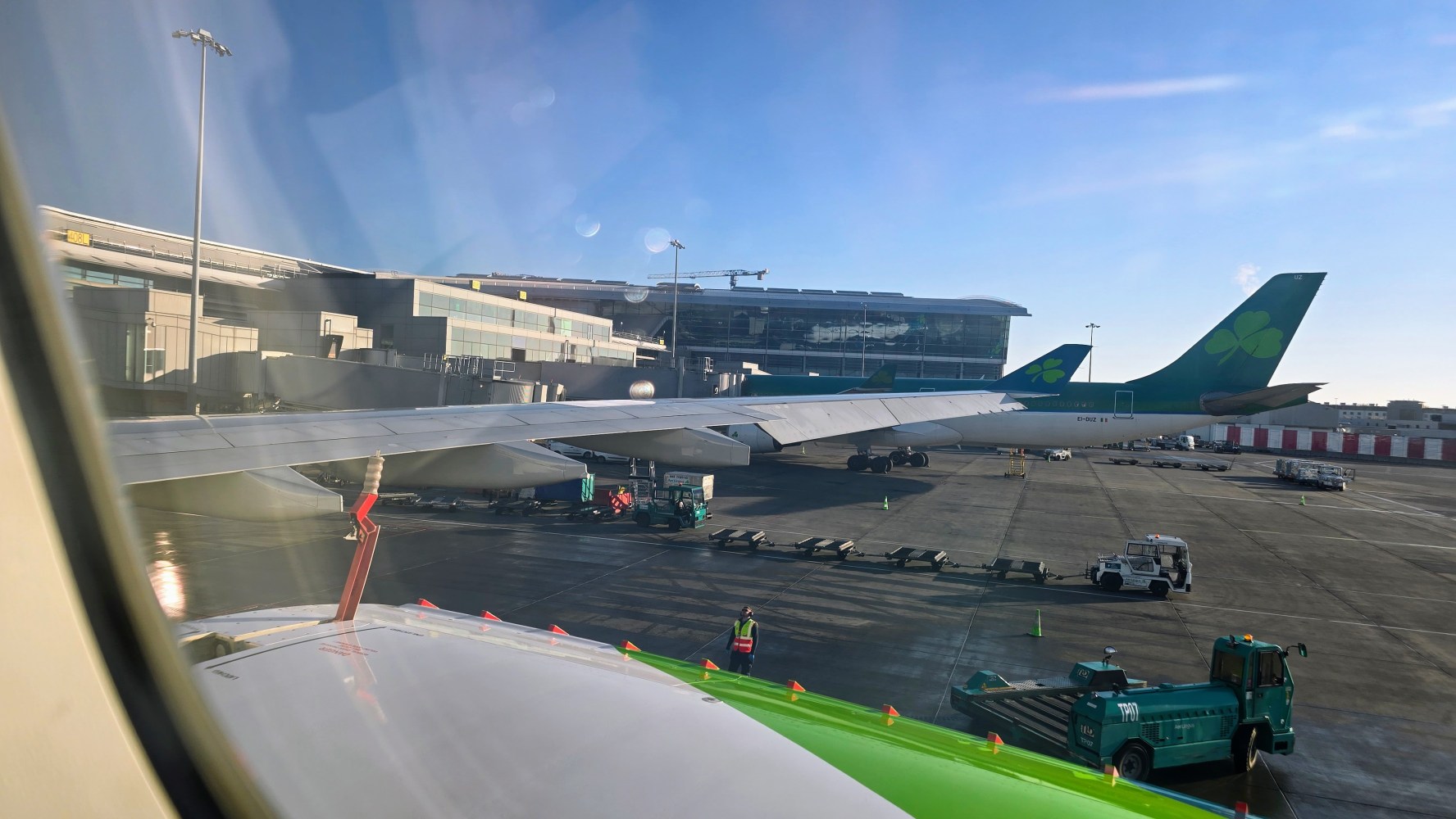 View from airplane window showing wing, other planes, and airport terminal on a sunny day.