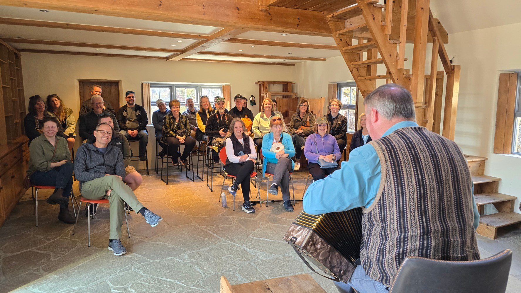Man playing an accordion in front of a seated audience in a rustic room.