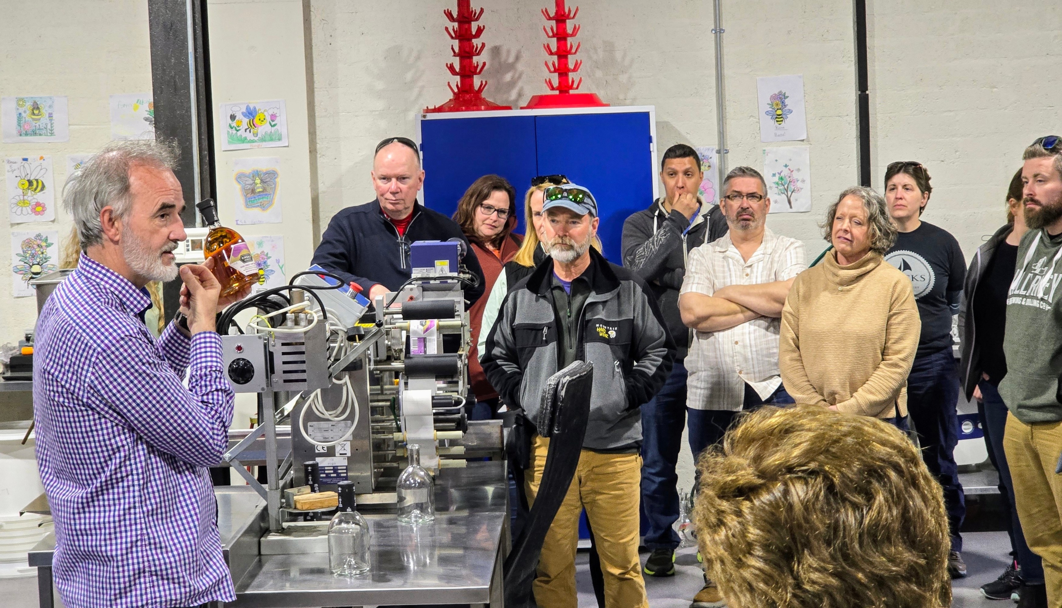 Man explaining a machine to a group of attentive people in a workshop.