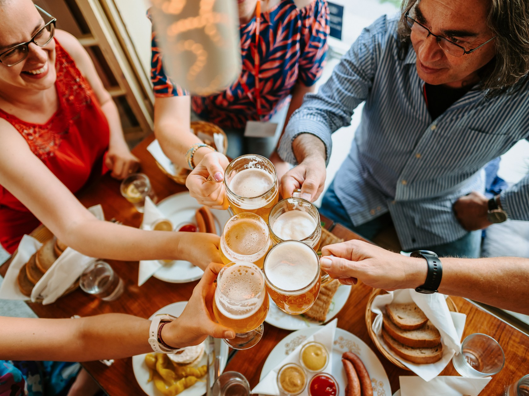 People clinking beer mugs over a table with food in a lively setting.