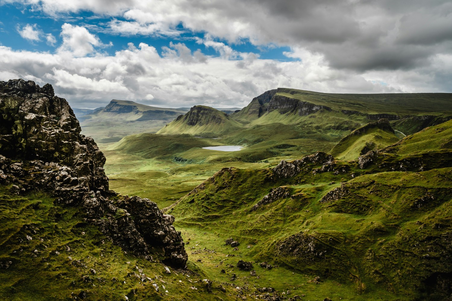 Scenic view of rocky, green hills under a cloudy sky with distant mountains.