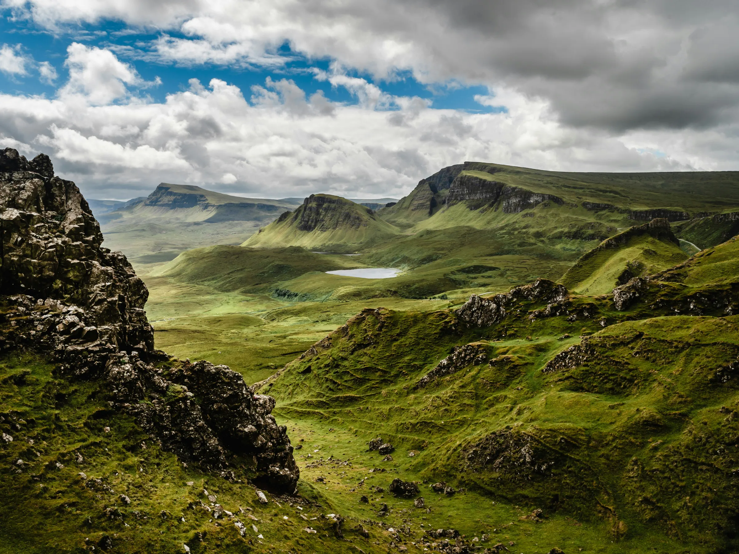 Scenic view of rocky, green hills under a cloudy sky with distant mountains.