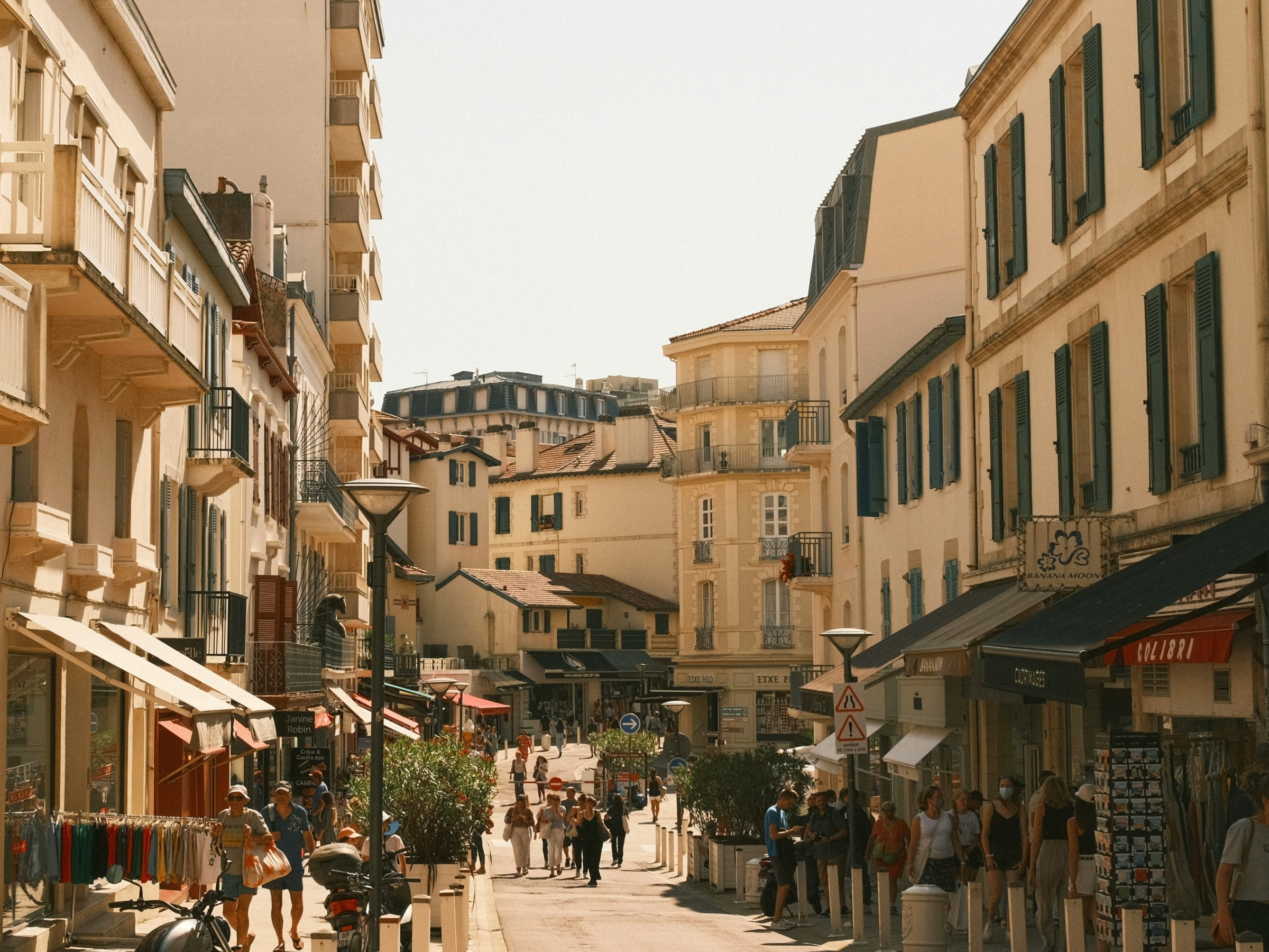 Pedestrian street with shops, people, and motorcycles in a sunny European town.