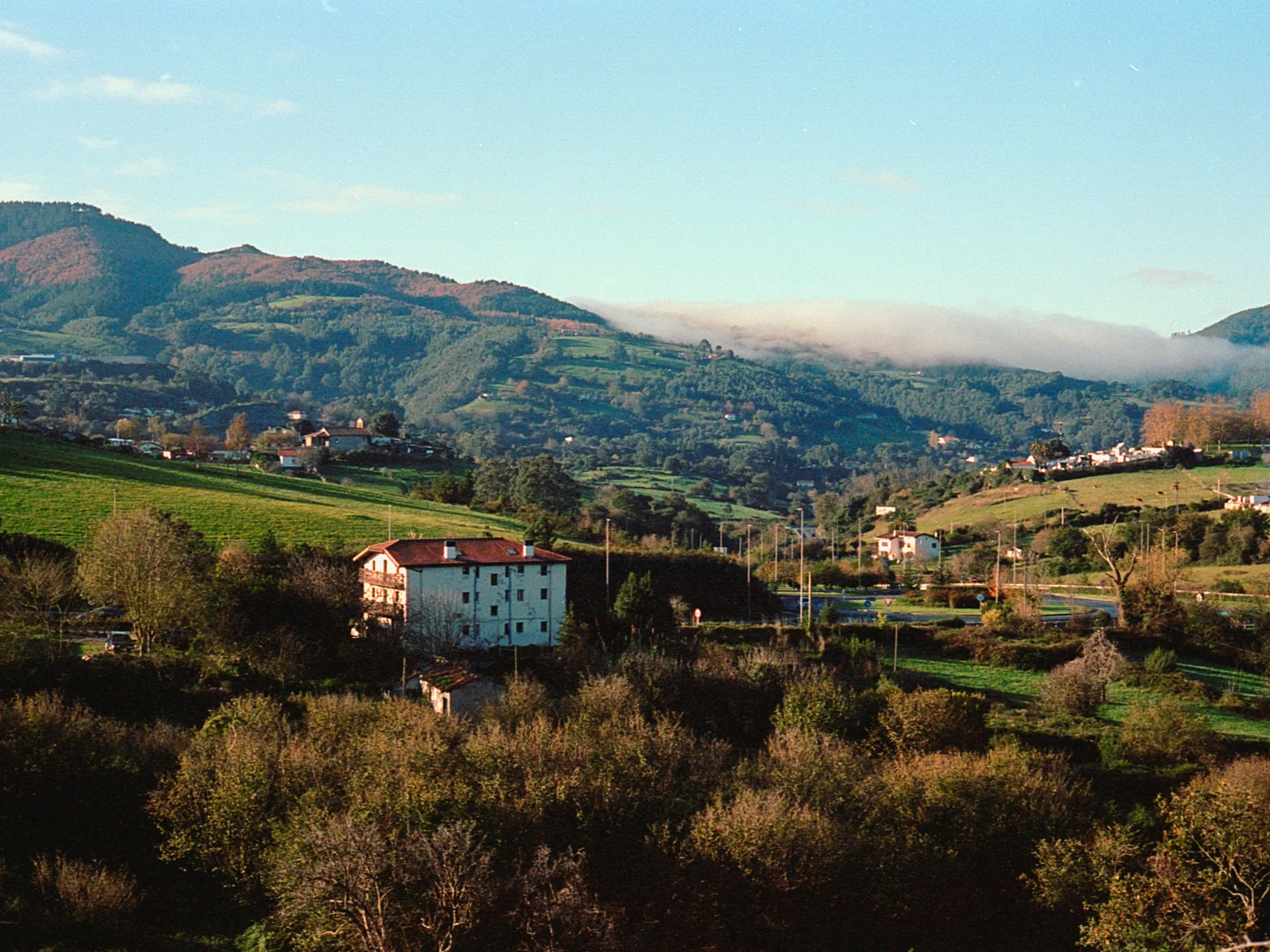 Countryside landscape with hills, scattered houses, and a large white building in the foreground.