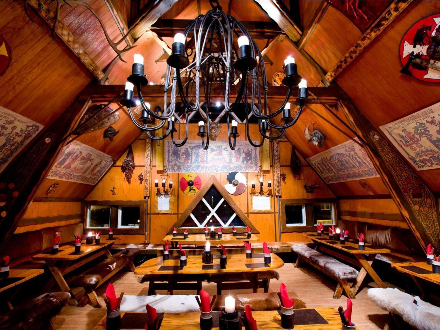 Rustic dining room with wooden tables, benches, and a large chandelier under a sloped ceiling.
