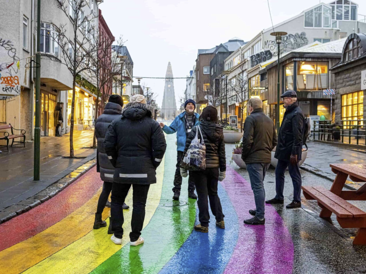 Group of people standing on a rainbow-painted street in an urban setting.