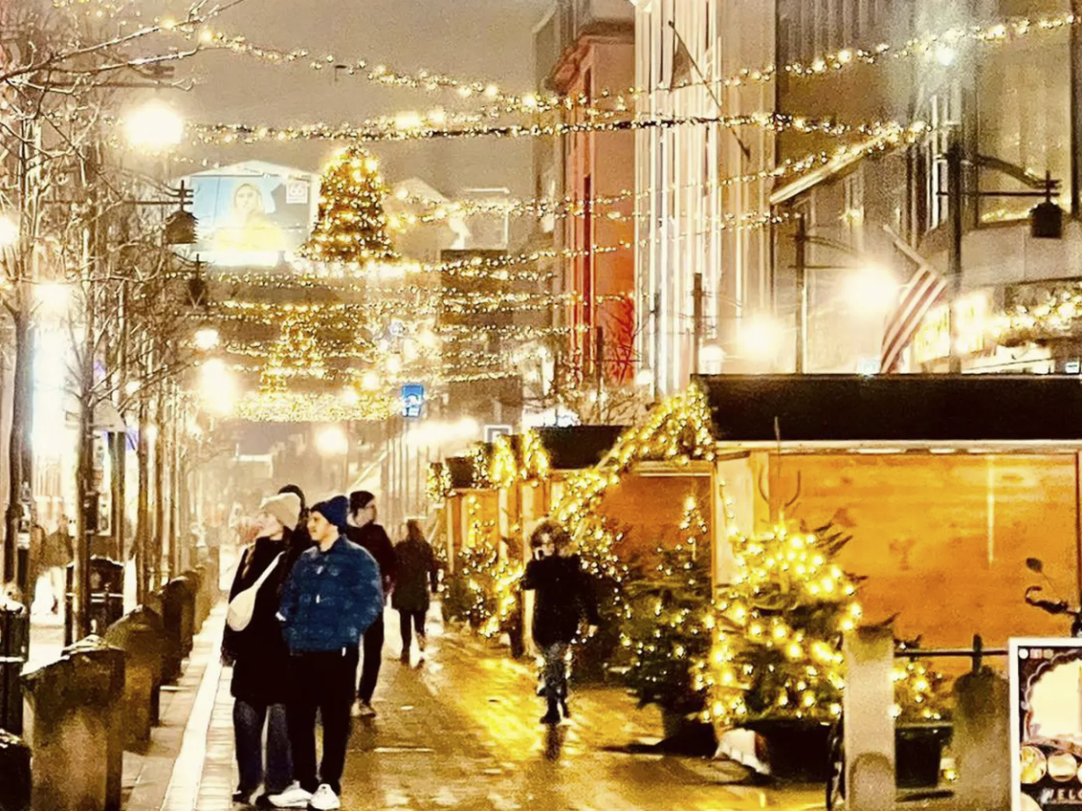 Festive street with Christmas lights, people, and decorated trees at night.