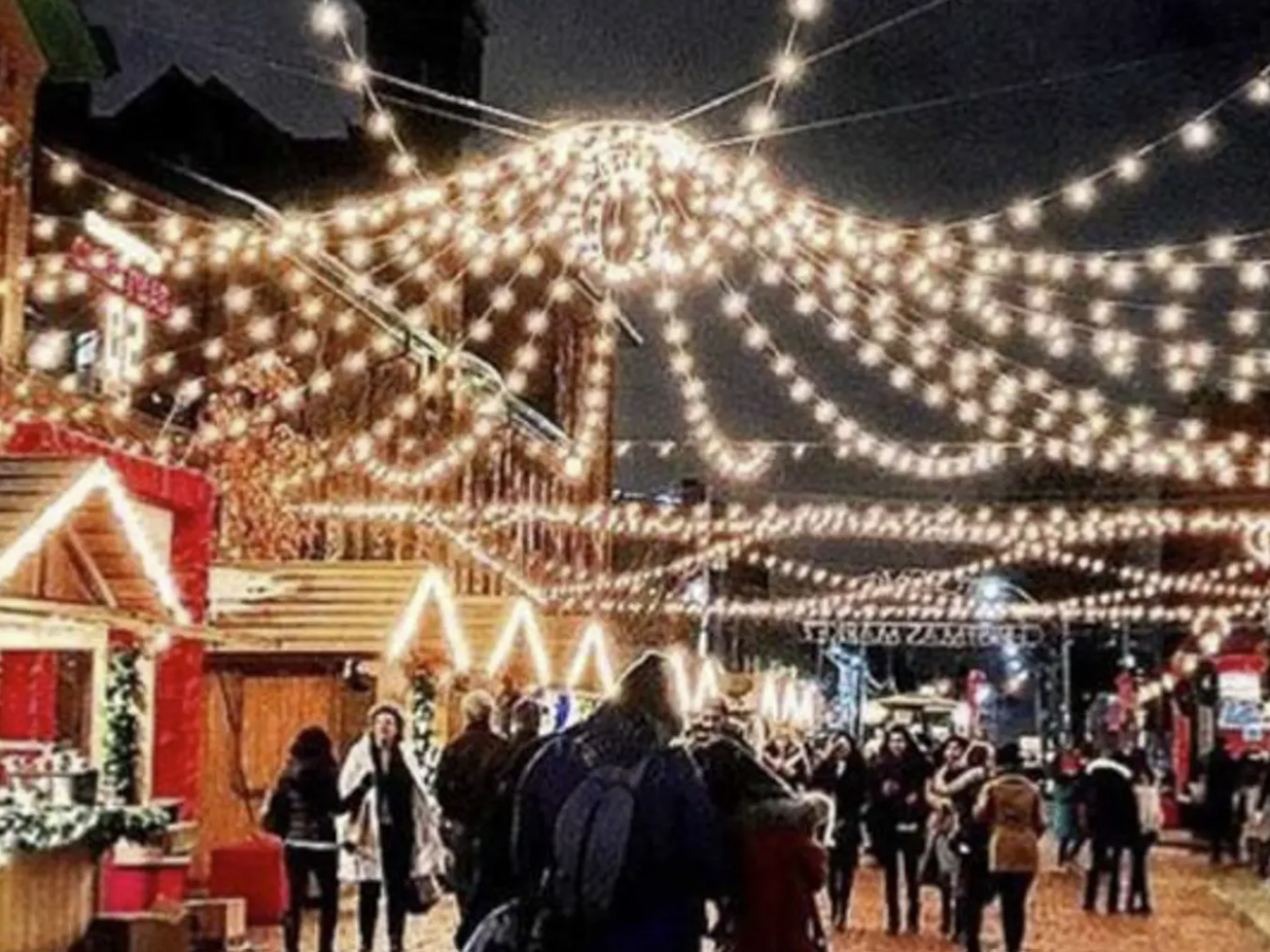Festive street market with string lights overhead and people walking at night.