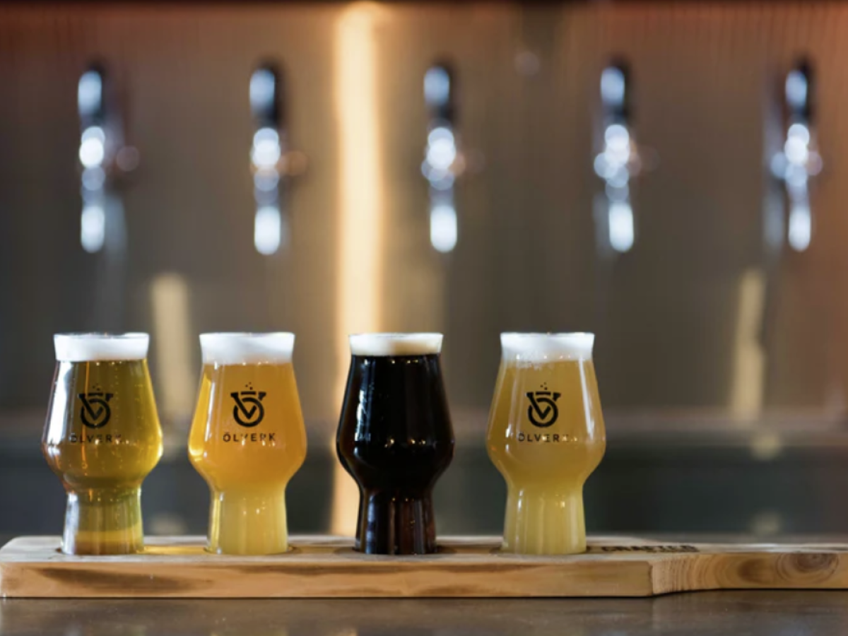 Four beer glasses on a wooden tray with a blurred bar background.