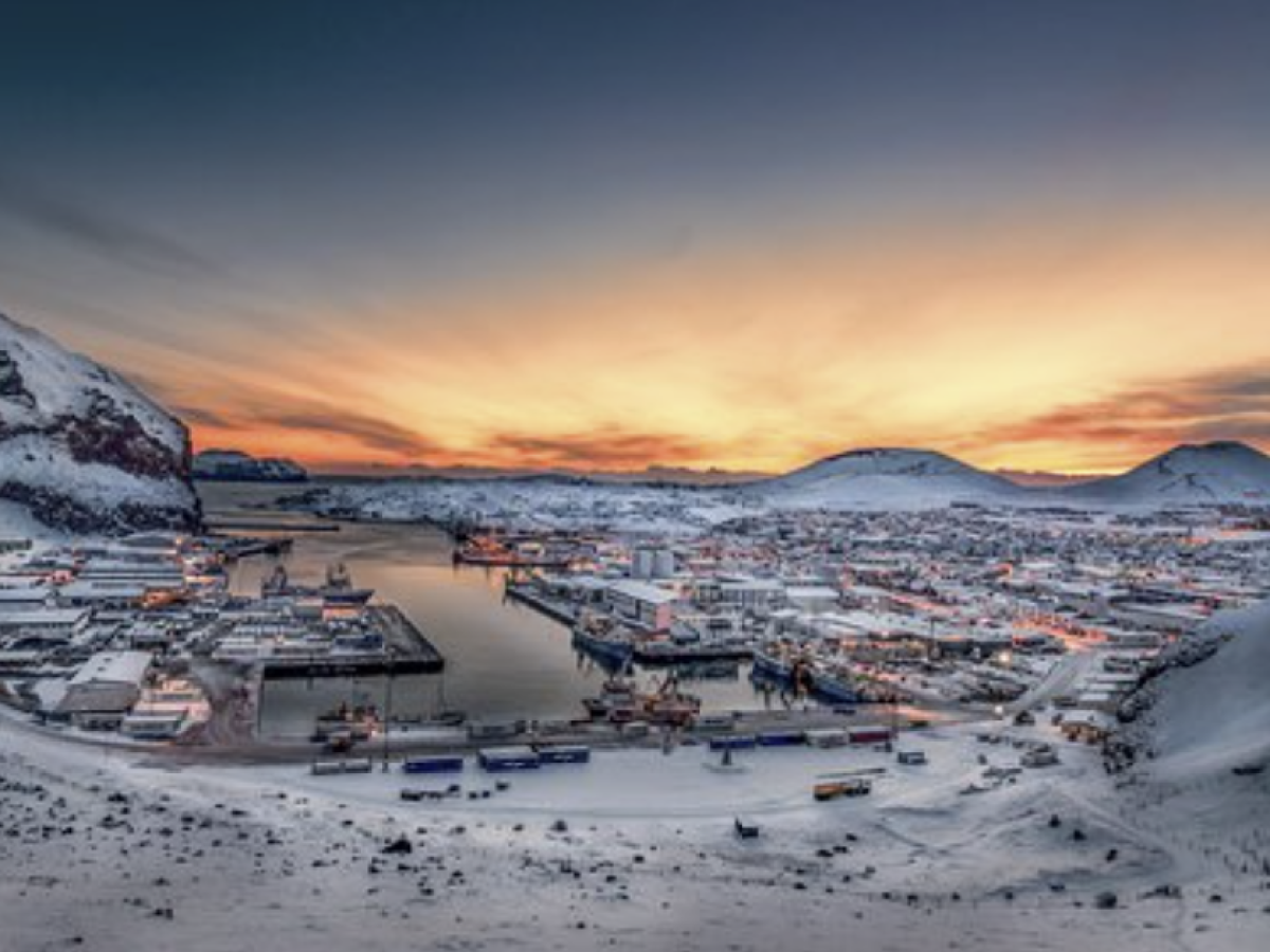 Snowy harbor town at sunset with mountains in the background.