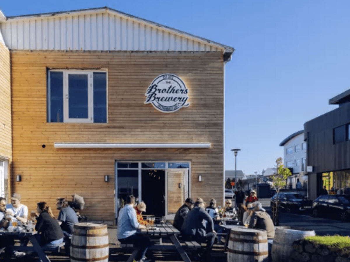 Outdoor seating at a brewery with wooden exterior and people enjoying drinks under clear skies.
