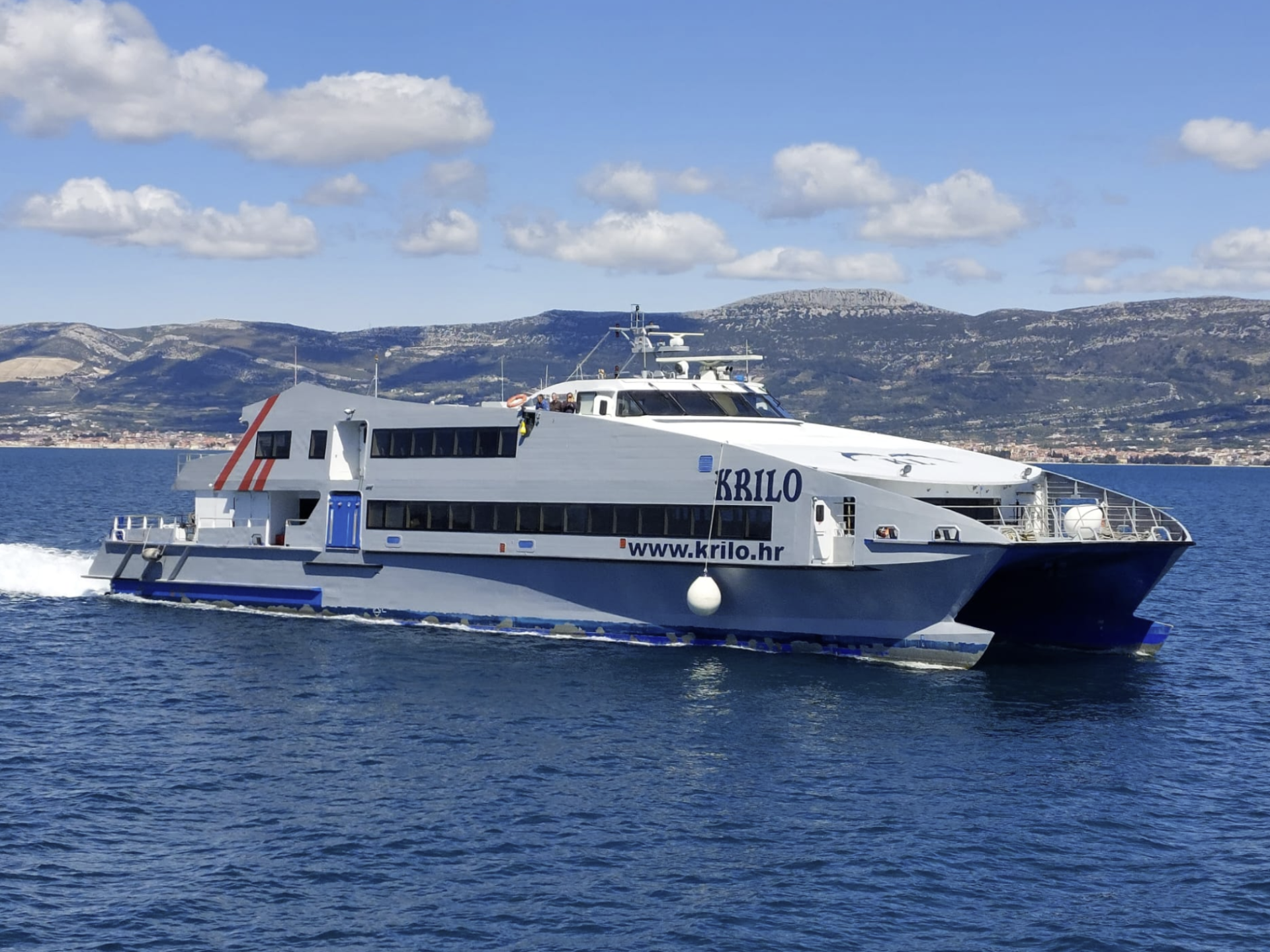 A ferry sailing on the ocean with mountains and clouds in the background.