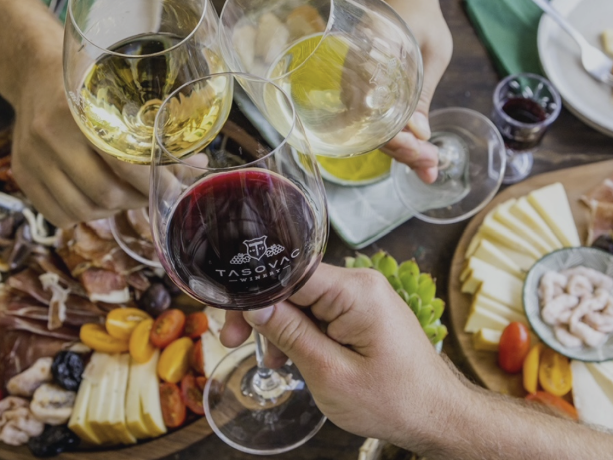 People toasting with wine glasses over a table with cheese and meats.