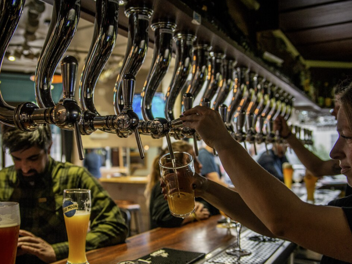 Bartender pouring beer from taps, patrons in background at a bar.