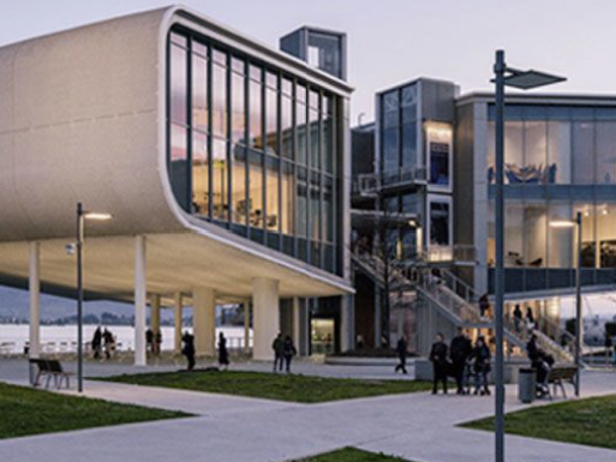 Modern building with large glass windows and curved design by the water at dusk.