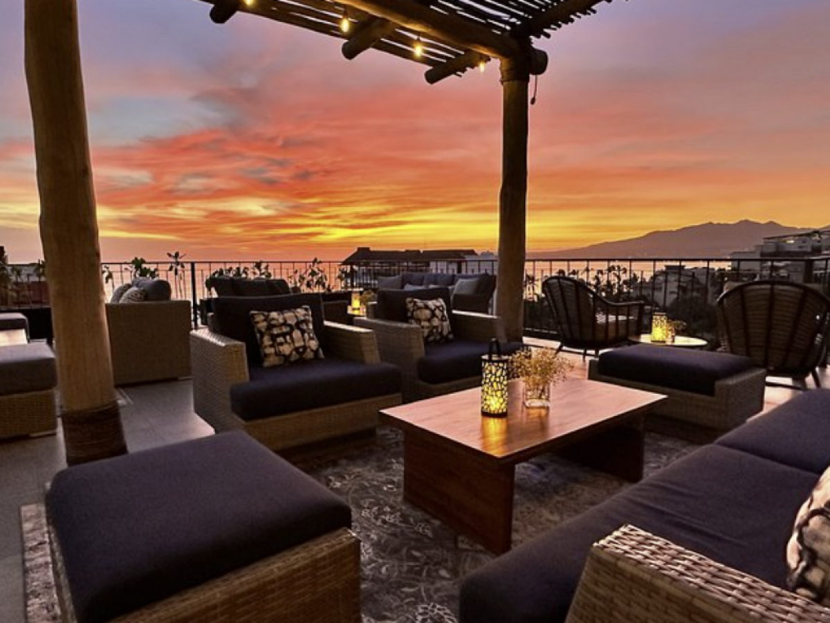 Outdoor seating under pergola with sunset view over cityscape.