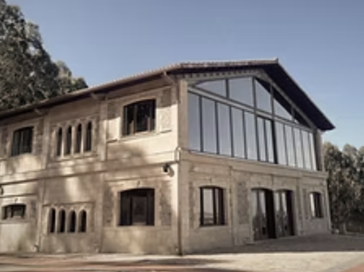 Two-story stone building with large windows, surrounded by trees.