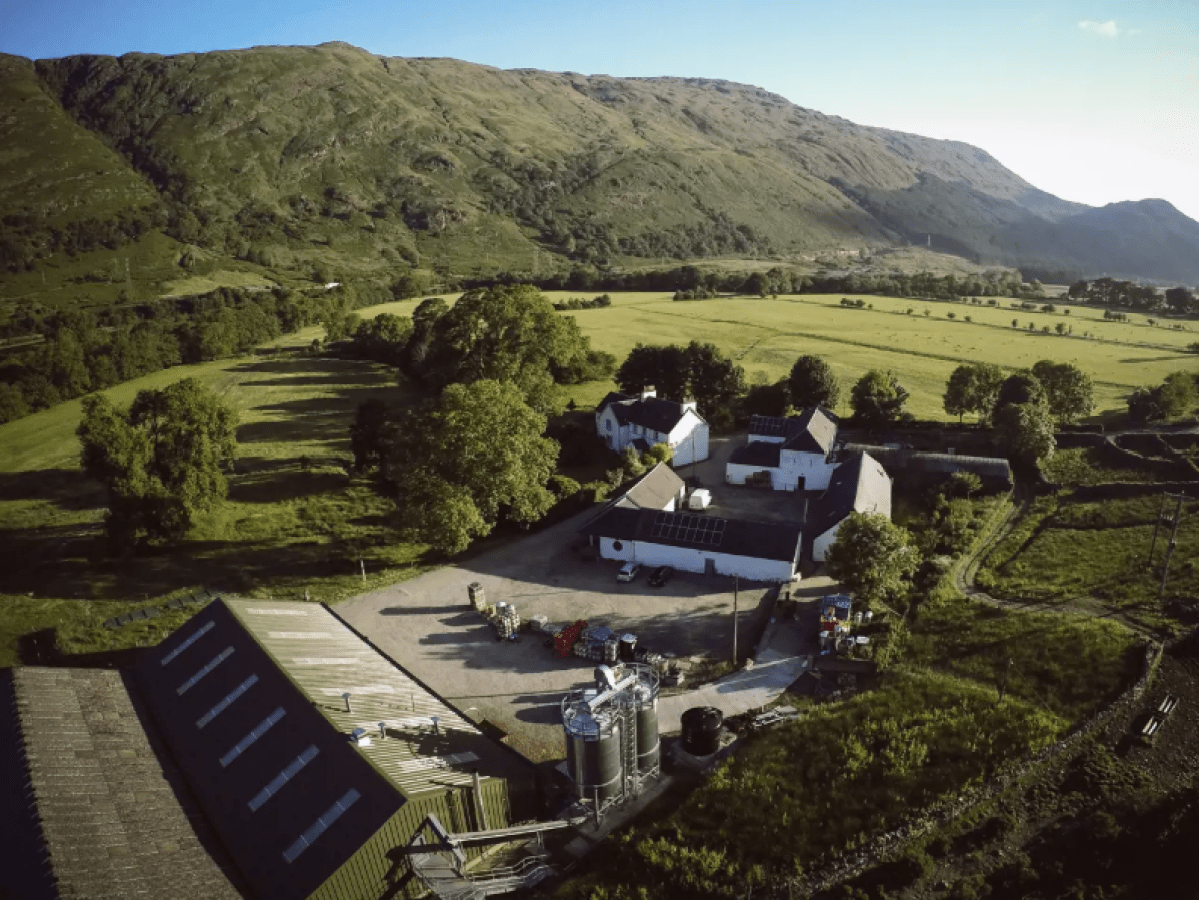 Aerial view of a farm with buildings, green fields, and mountains.