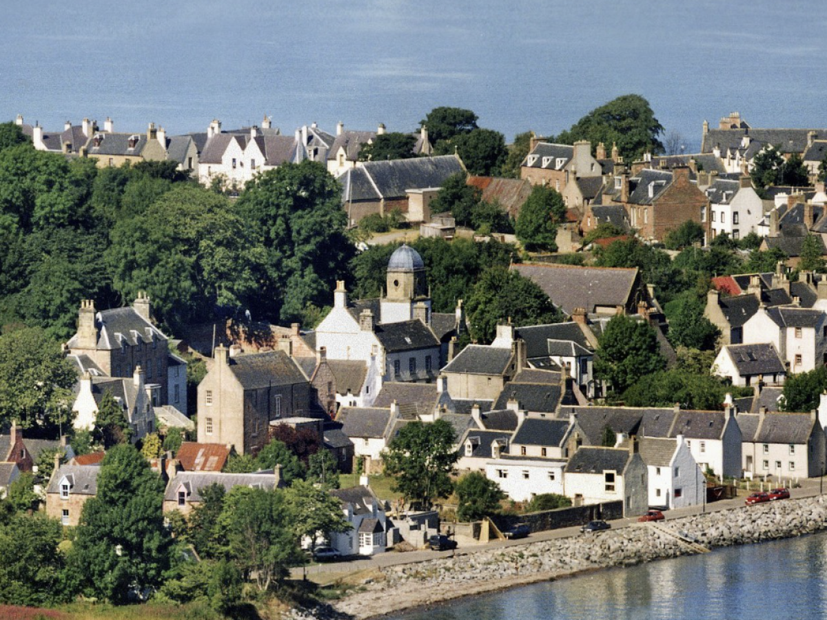 Charming coastal village with stone houses by the water, surrounded by lush greenery.