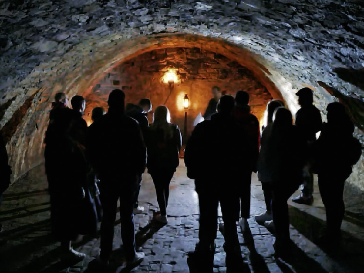 Group of people silhouetted in a dimly lit stone archway with a warm light.