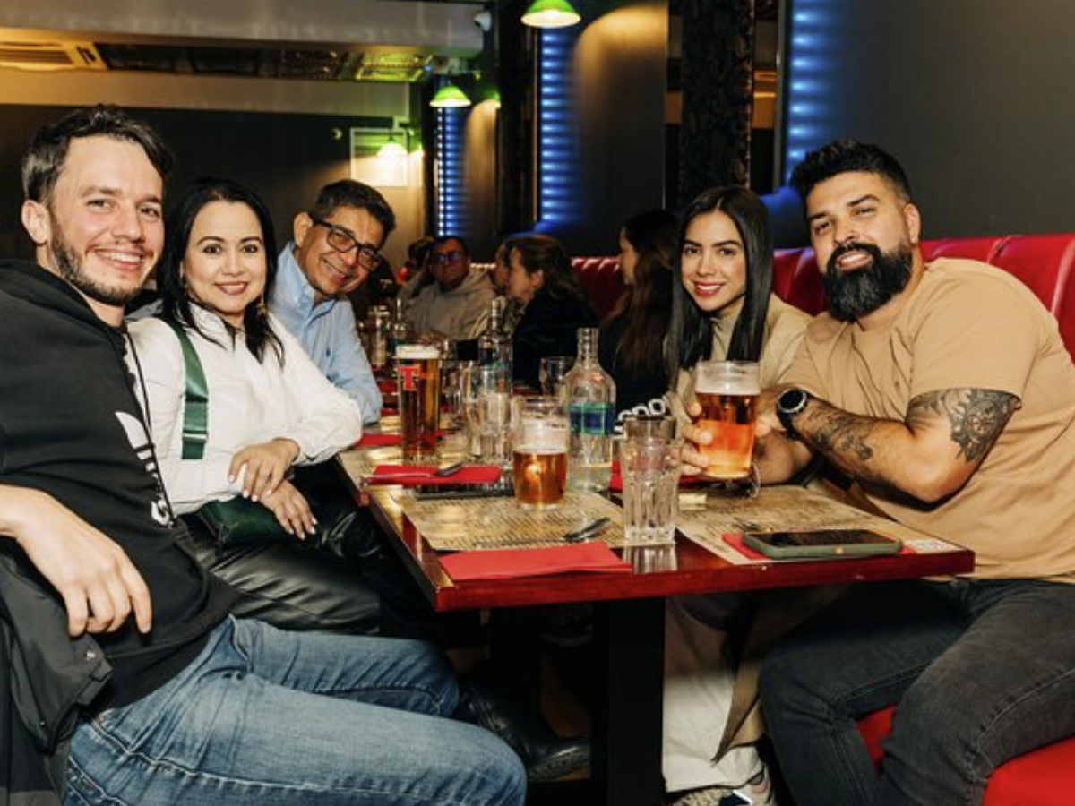 Five people sitting at a restaurant table with drinks, smiling at the camera.