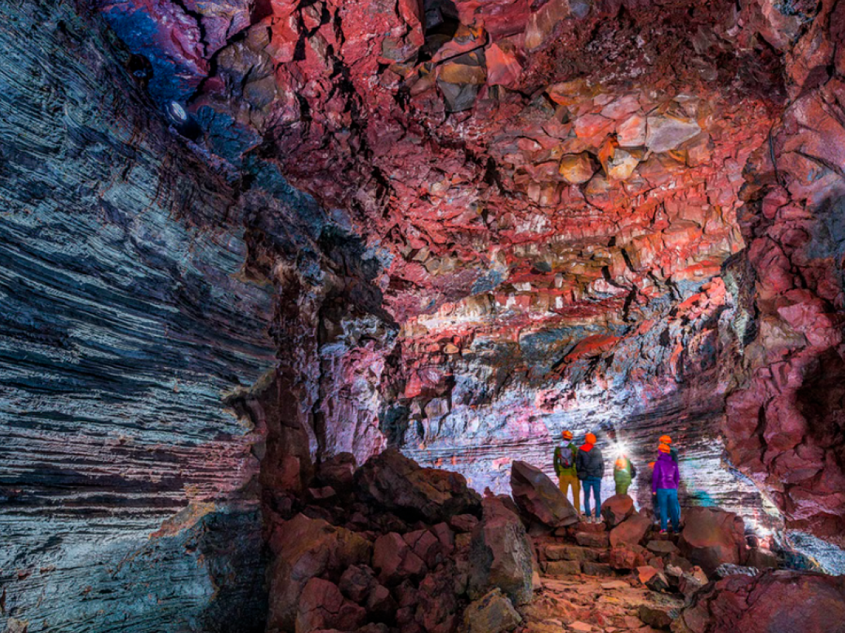People wearing helmets explore a colorful, rocky cave with layered walls and a textured ceiling.
