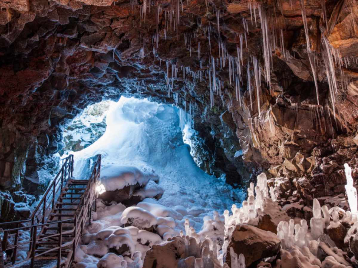 Ice cave with snow, icicles, and a metal staircase leading out.