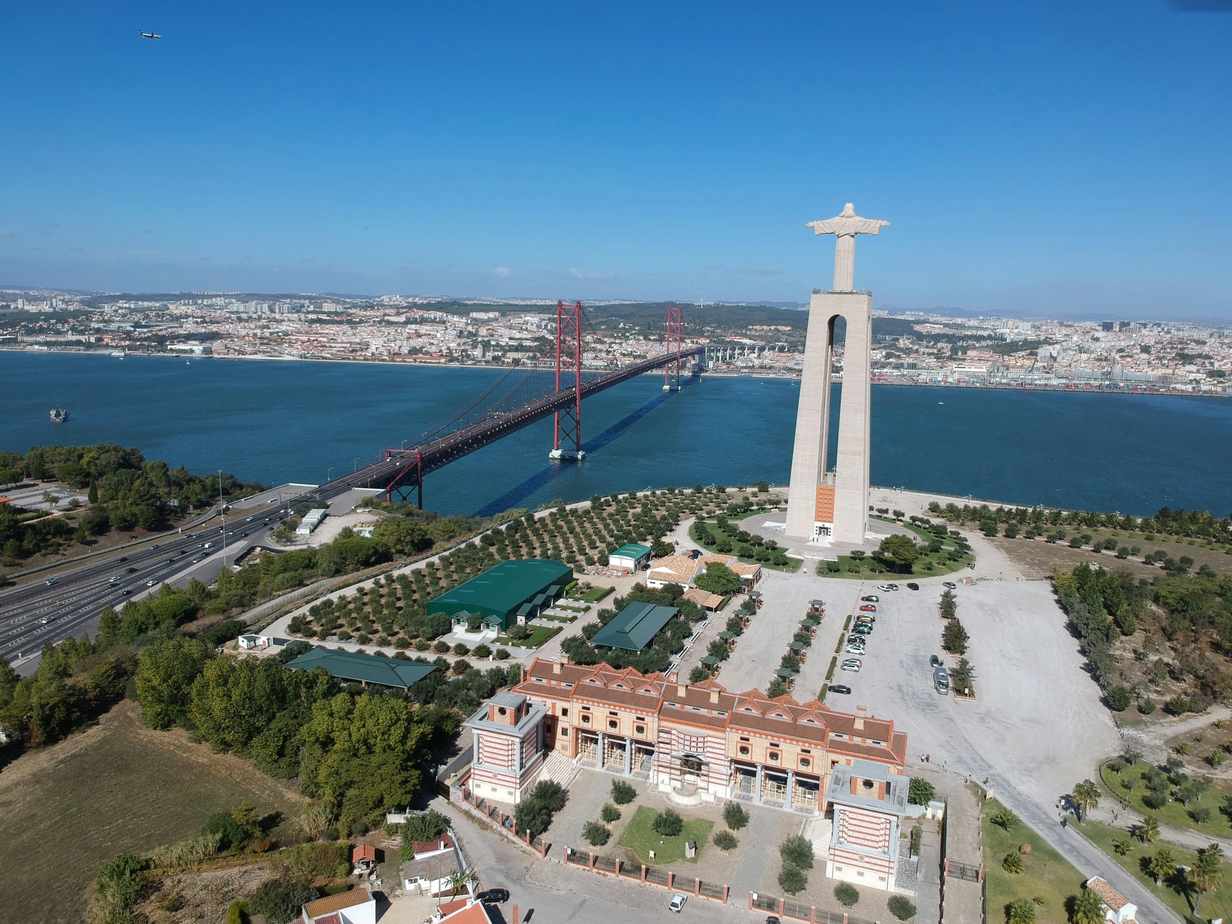 Aerial view of a large statue and a bridge over a wide river in a cityscape.