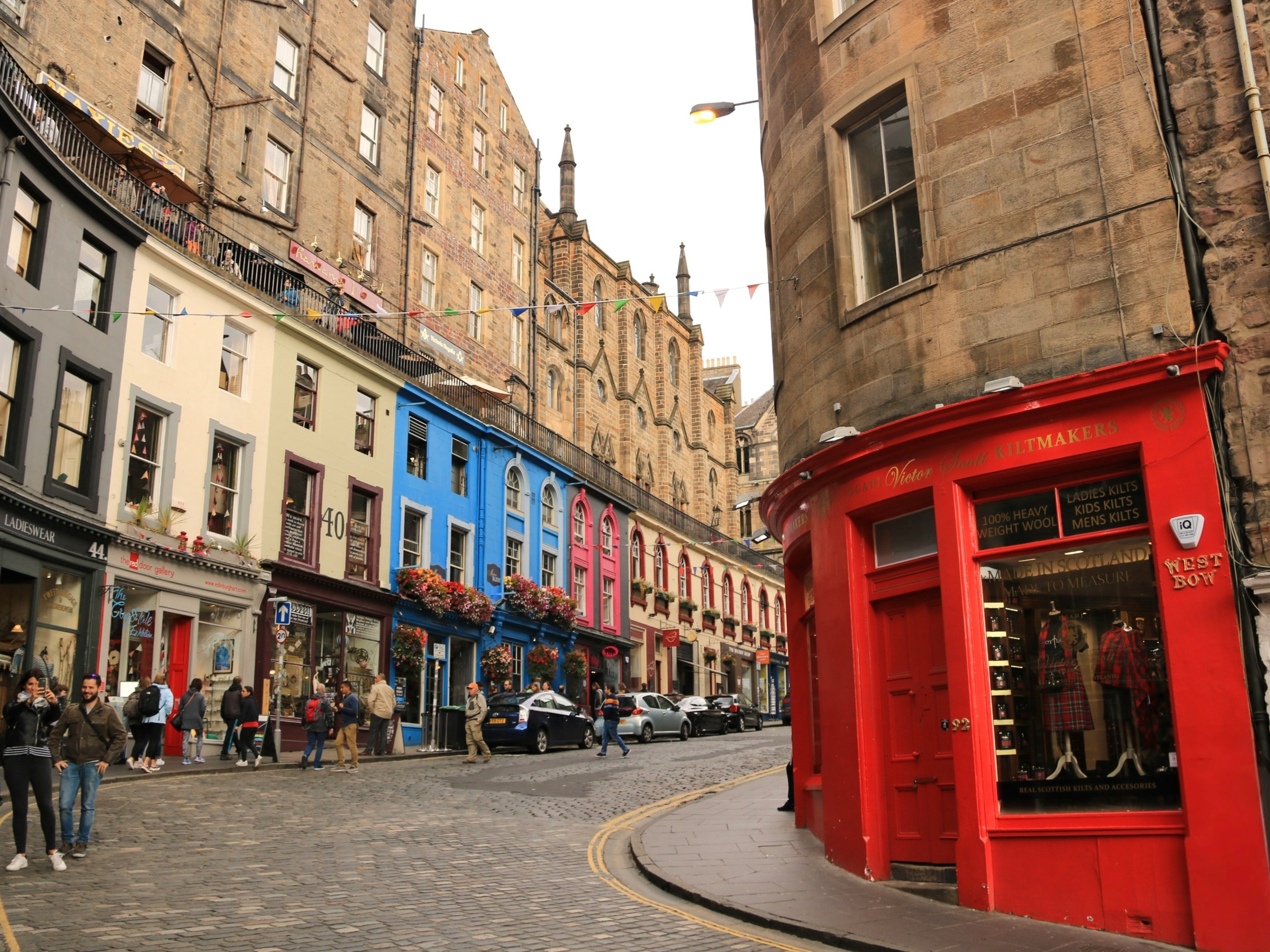 Colorful shops on a curved, cobblestone street with a red corner building.