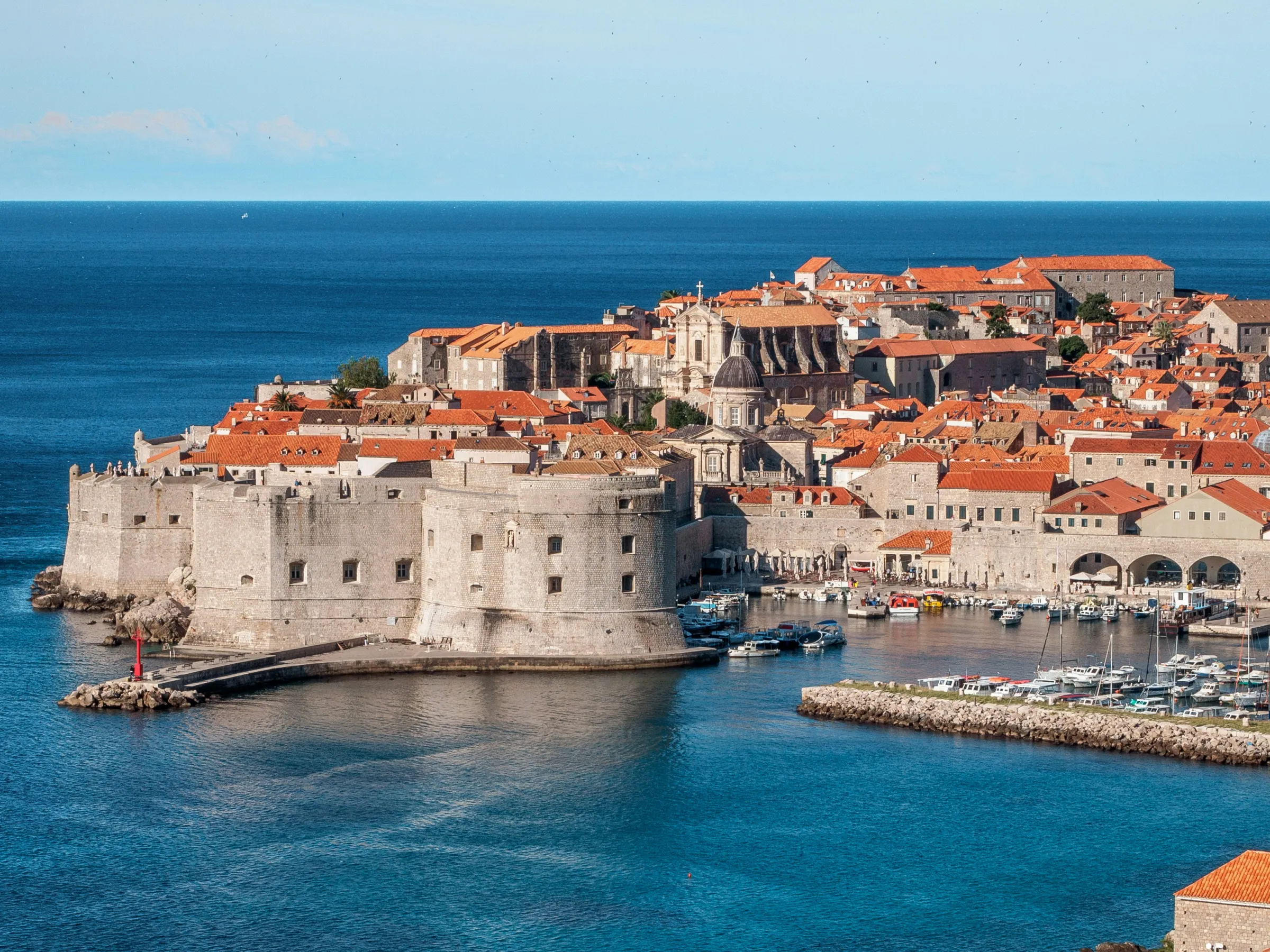 Historic coastal city with stone walls and red-tiled roofs by the sea.