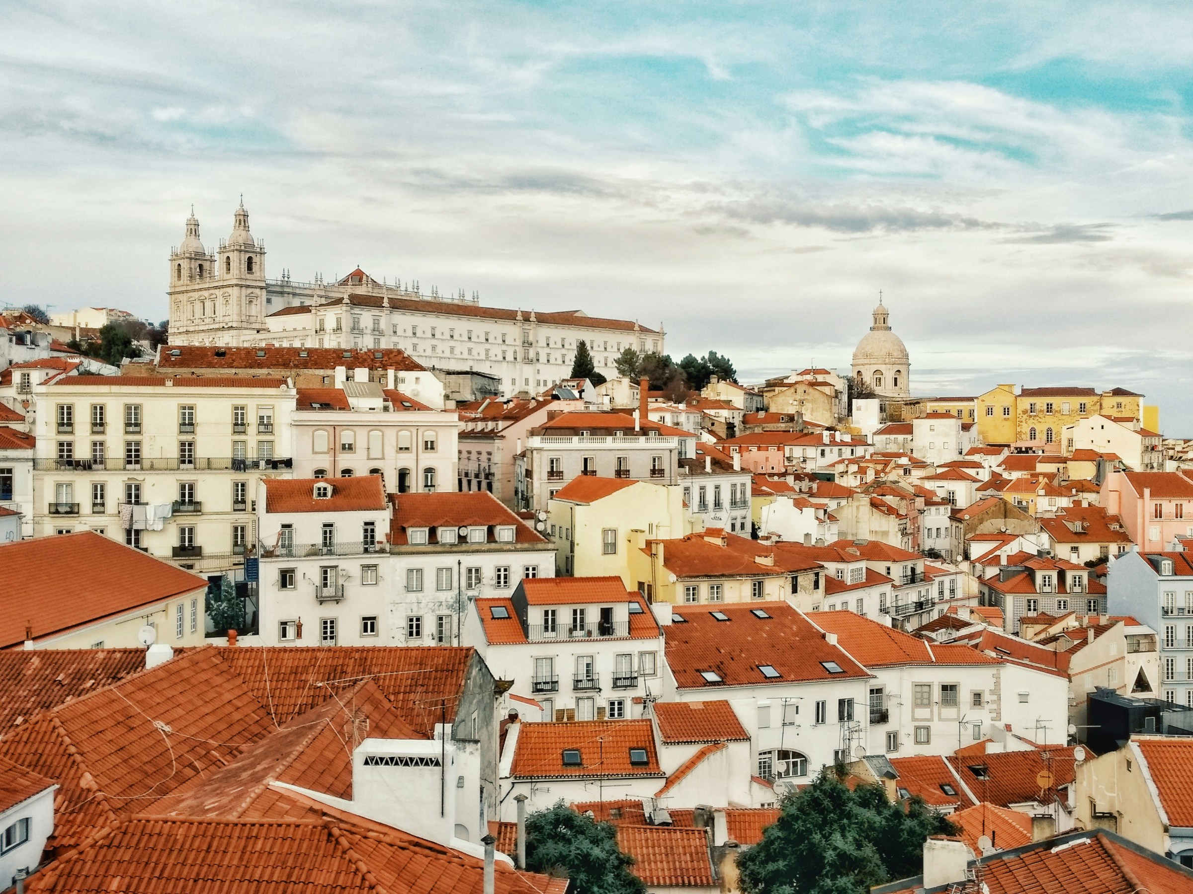 Panoramic view of Lisbon with red rooftops and historic buildings under a cloudy sky.