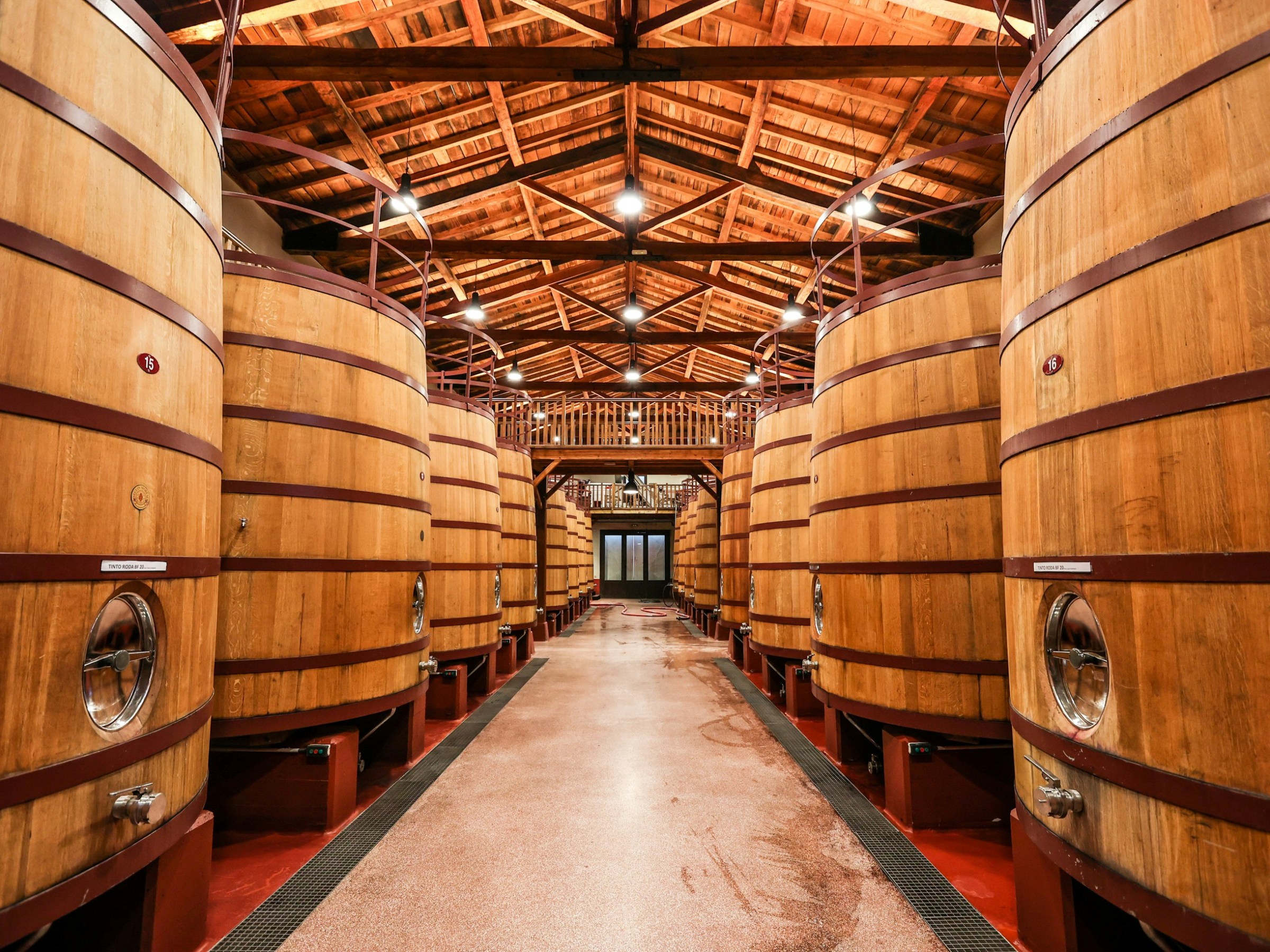 Interior of a winery with large wooden fermentation tanks and a wooden ceiling.