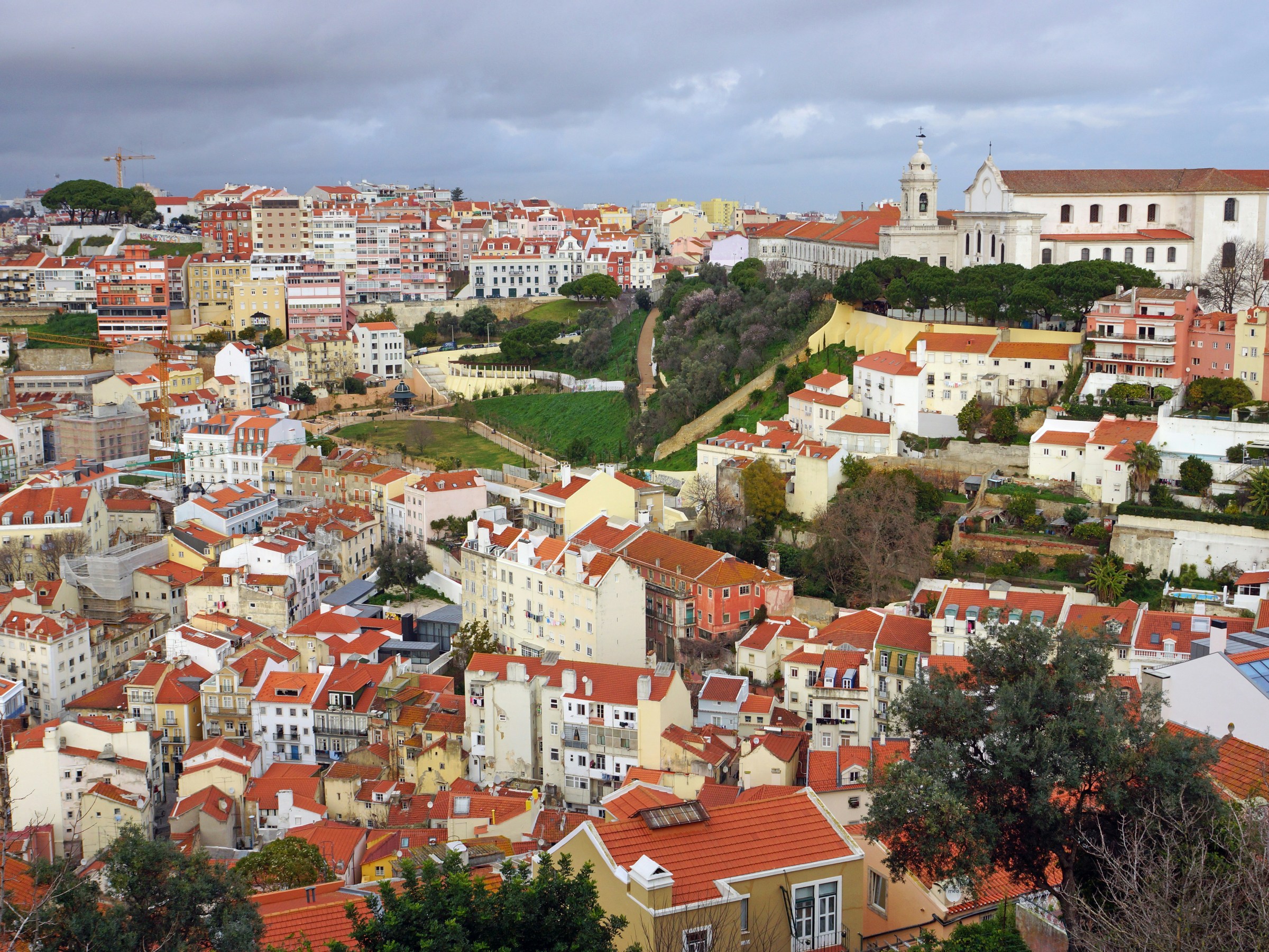Aerial view of Lisbon's colorful rooftops and historic buildings under a cloudy sky.