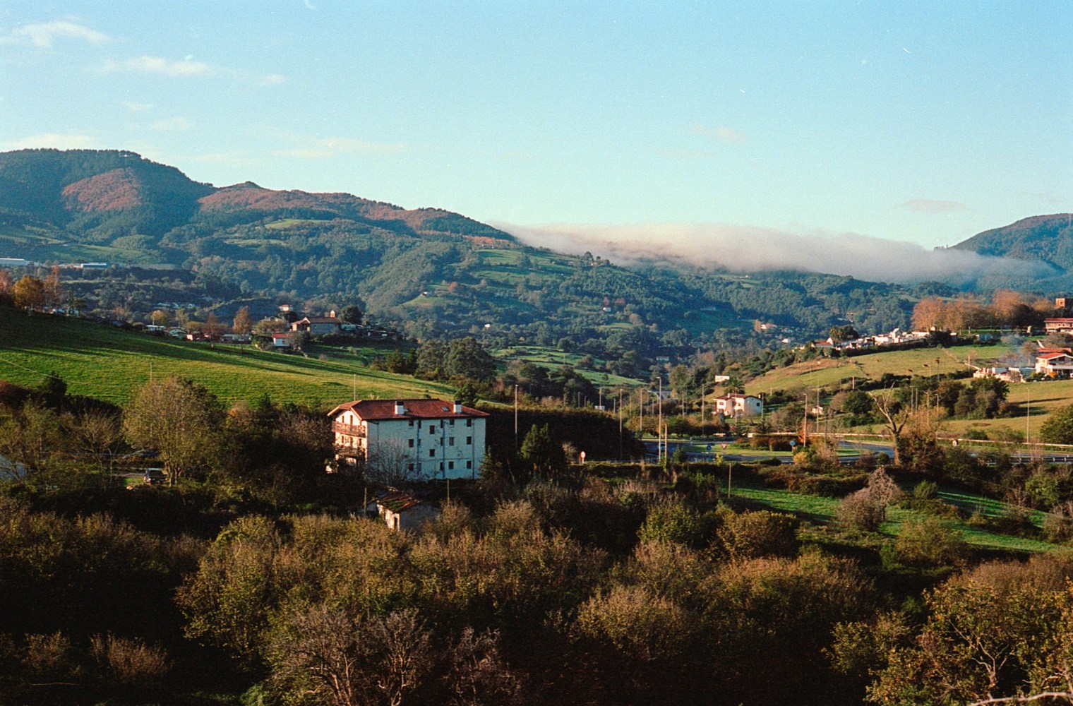 Scenic view of lush green hills with houses and mountains under a clear blue sky.