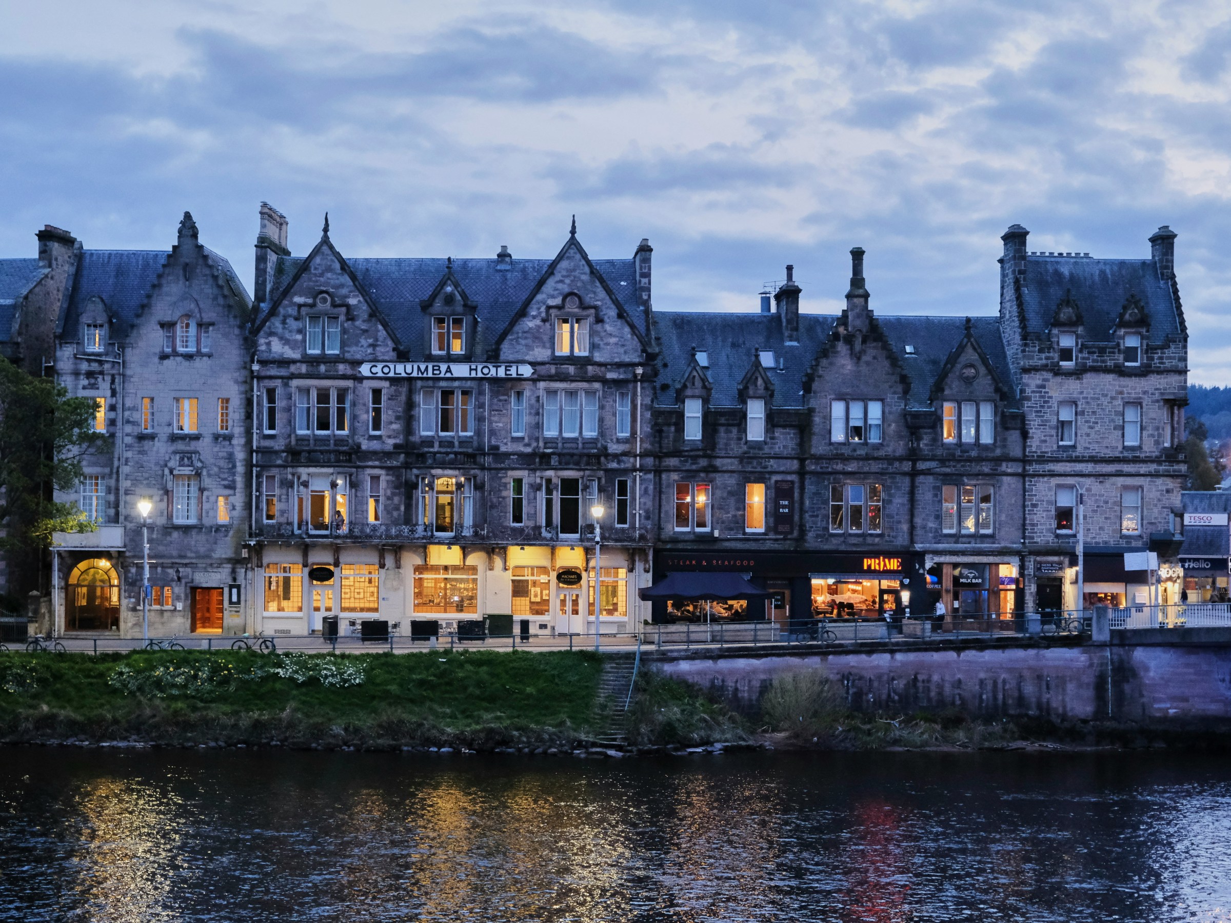 Historic hotel building along a river at dusk with illuminated windows.