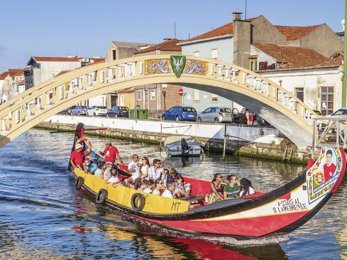 Boat with people on a canal under an arch bridge in a sunny cityscape.
