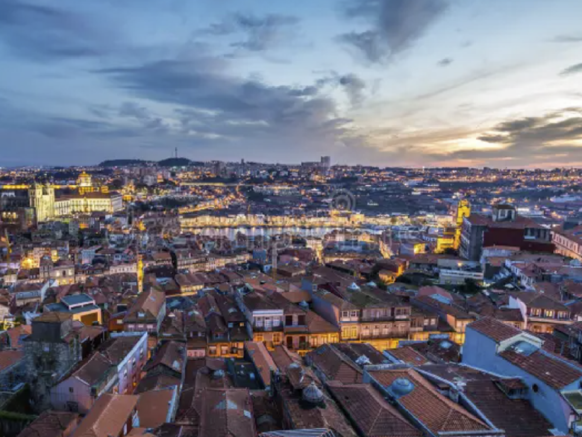 Aerial view of a cityscape at dusk with illuminated buildings and a cloudy sky.