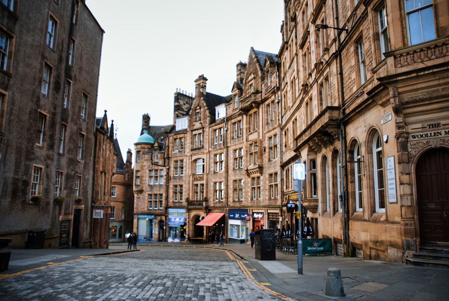 Historic stone buildings line a cobblestone street with a few pedestrians.