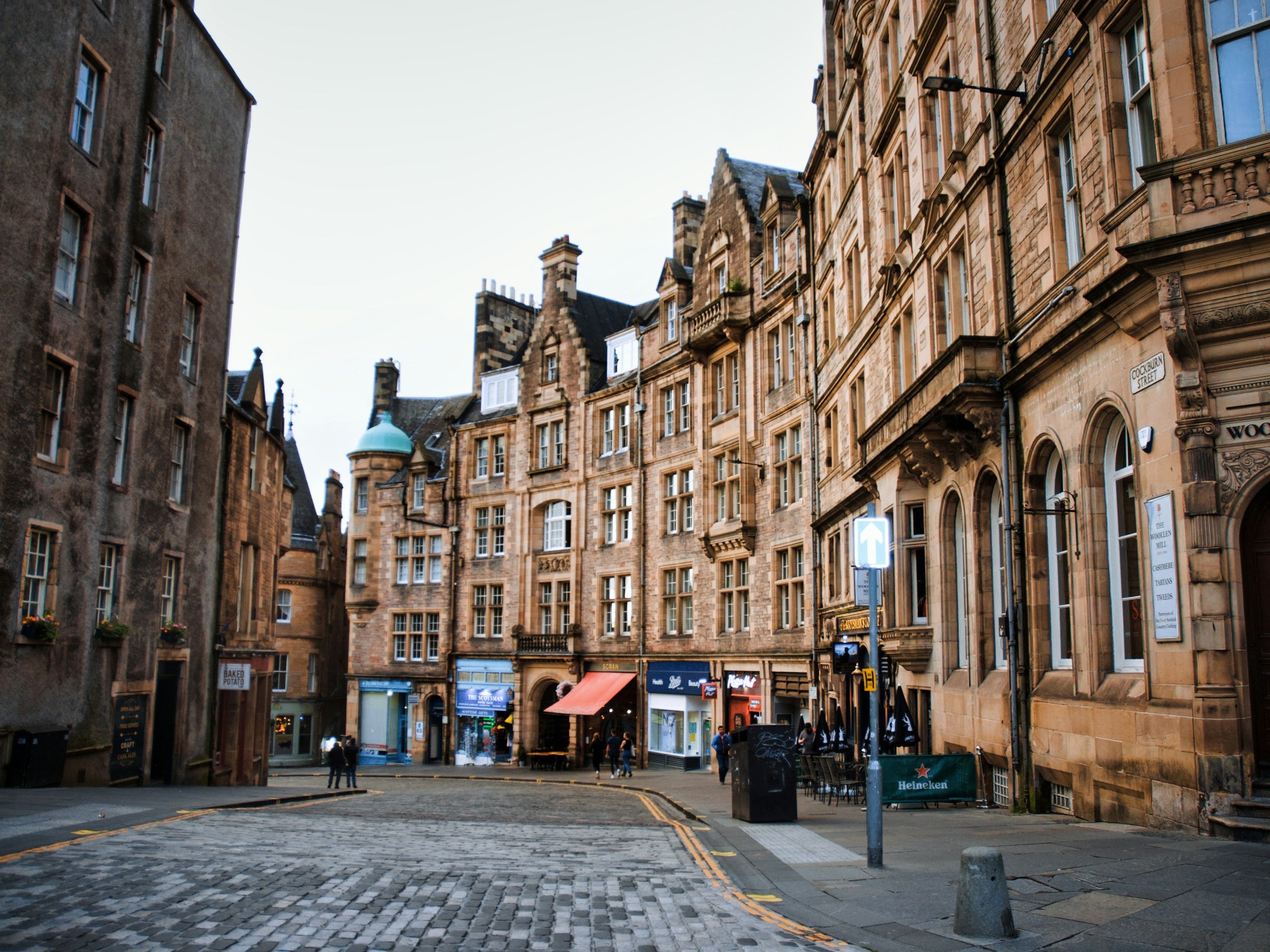 Historic stone buildings line a cobblestone street with a few pedestrians.