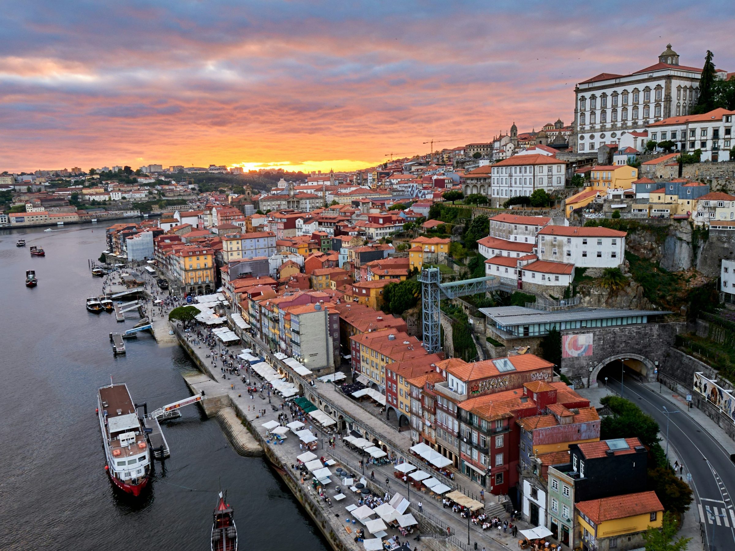 Aerial view of a riverside city at sunset with colorful buildings and boats.