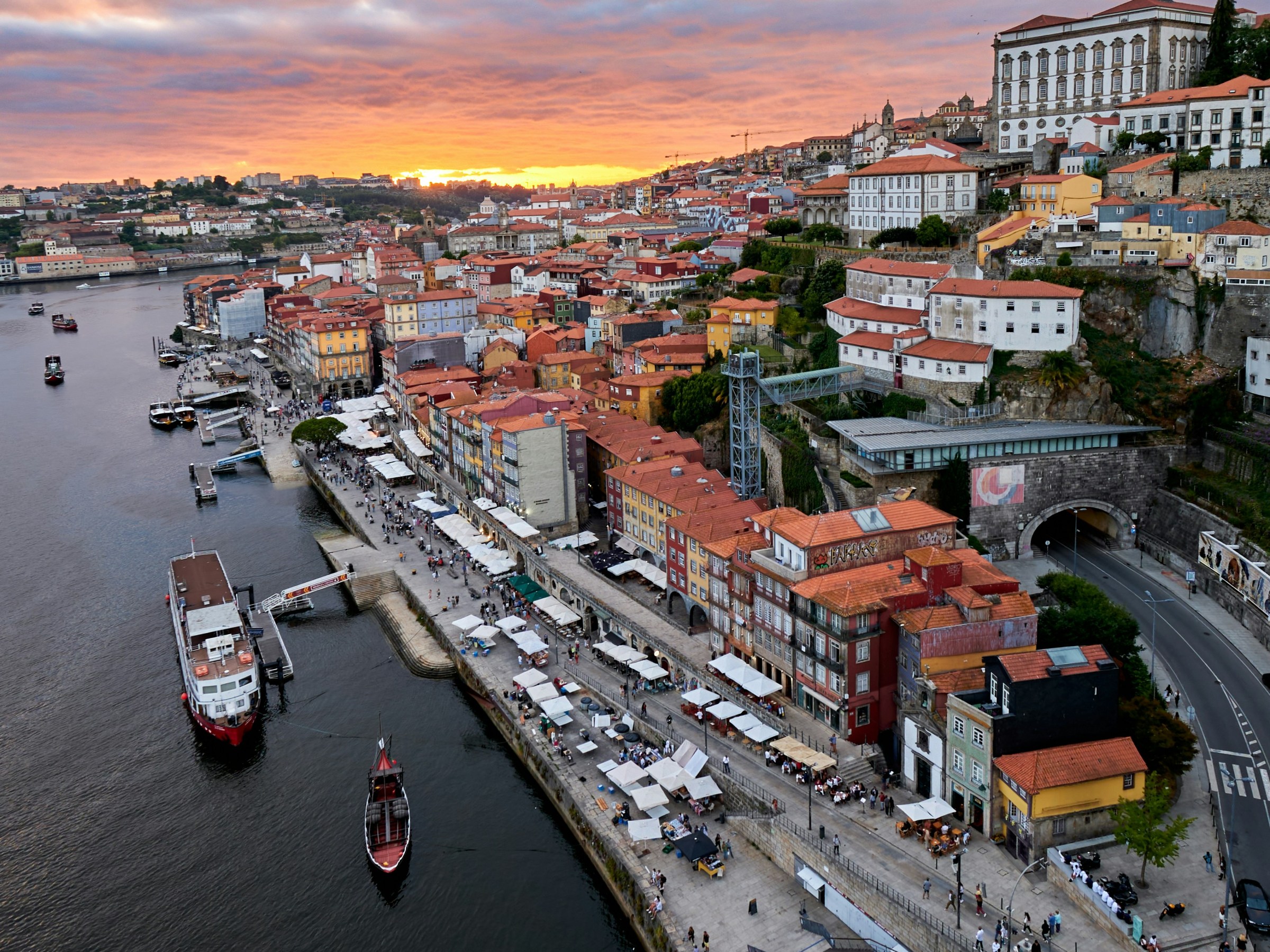Aerial view of a riverside city at sunset with colorful buildings and boats.