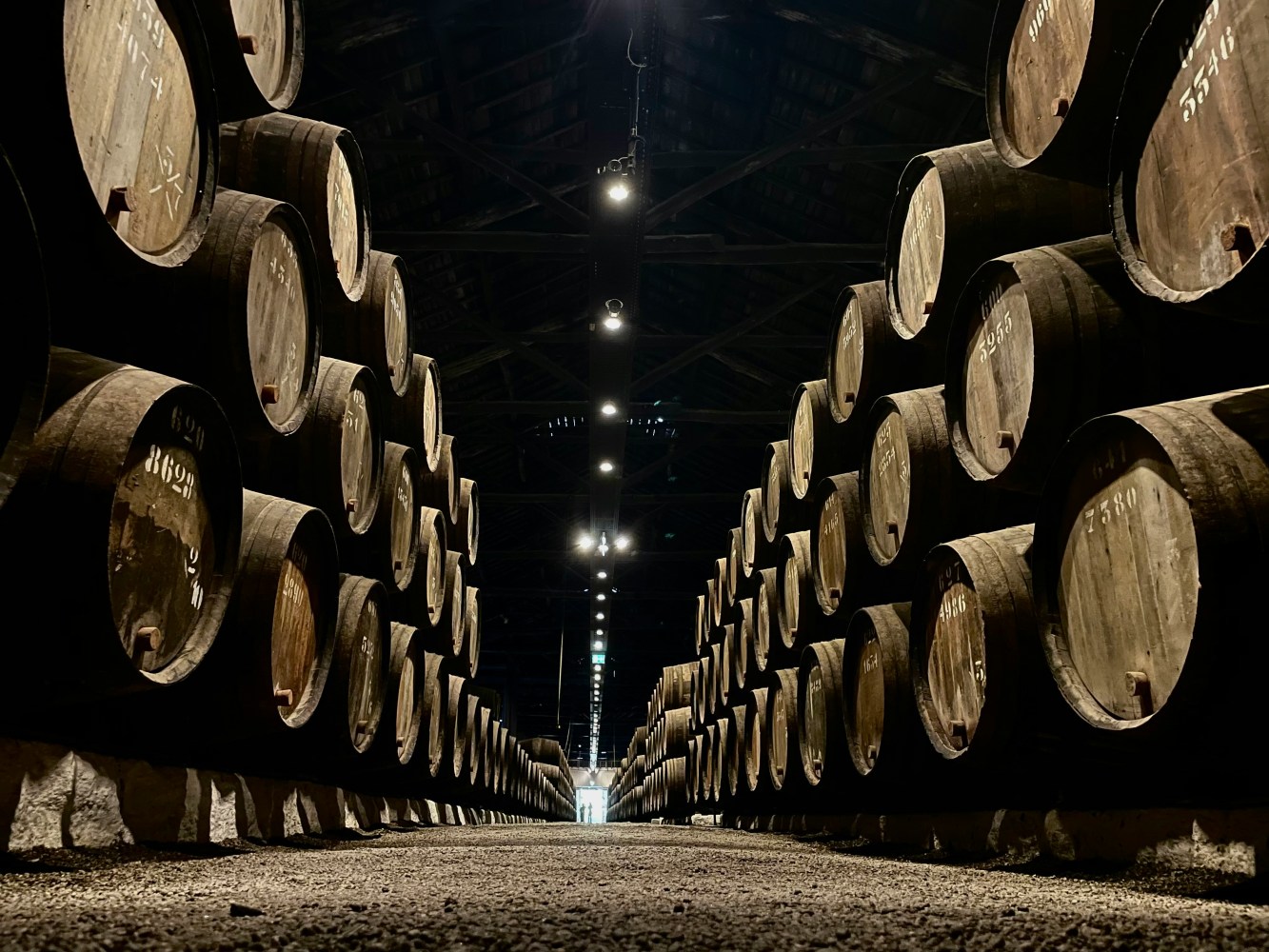 Rows of stacked wooden barrels in a dimly lit warehouse.