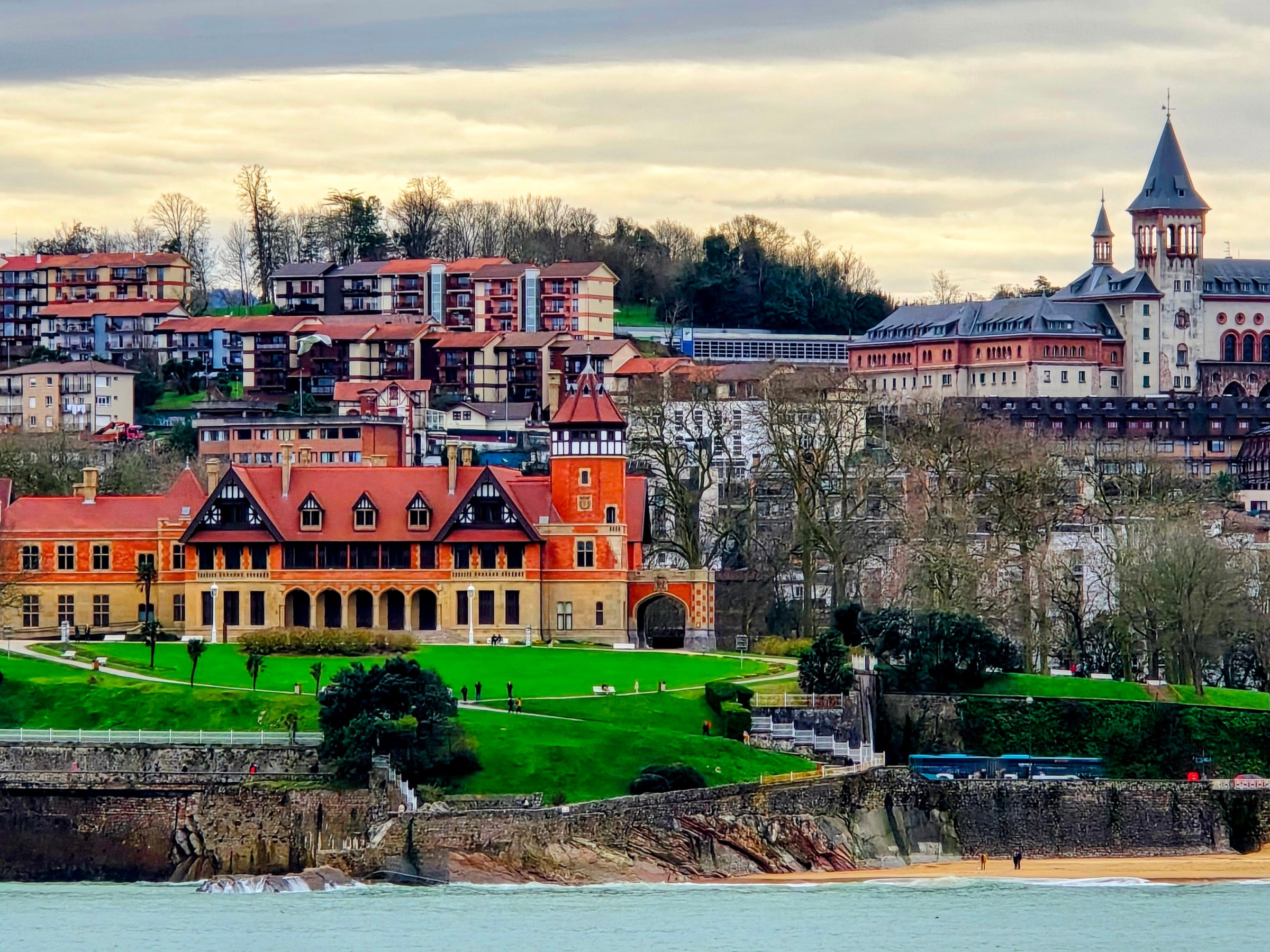 Scenic view of buildings and greenery by the sea on a cloudy day.