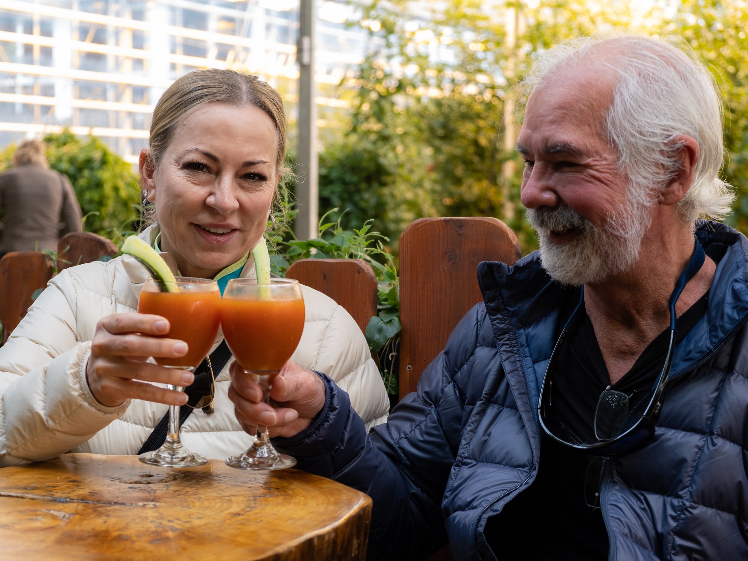 Smiling couple toasting with drinks outdoors on a wooden table.