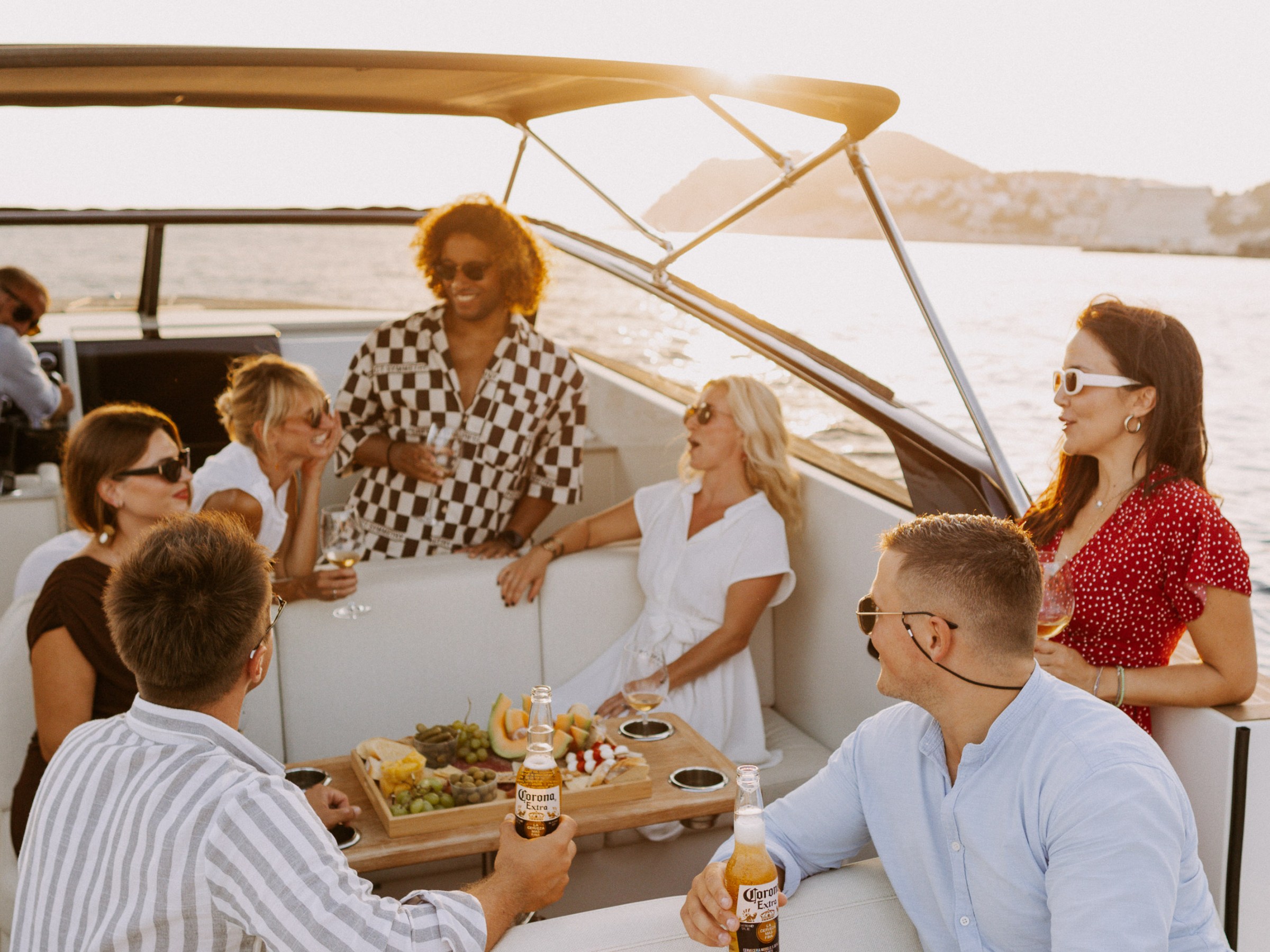 Group of friends on boat enjoying drinks and snacks at sunset.